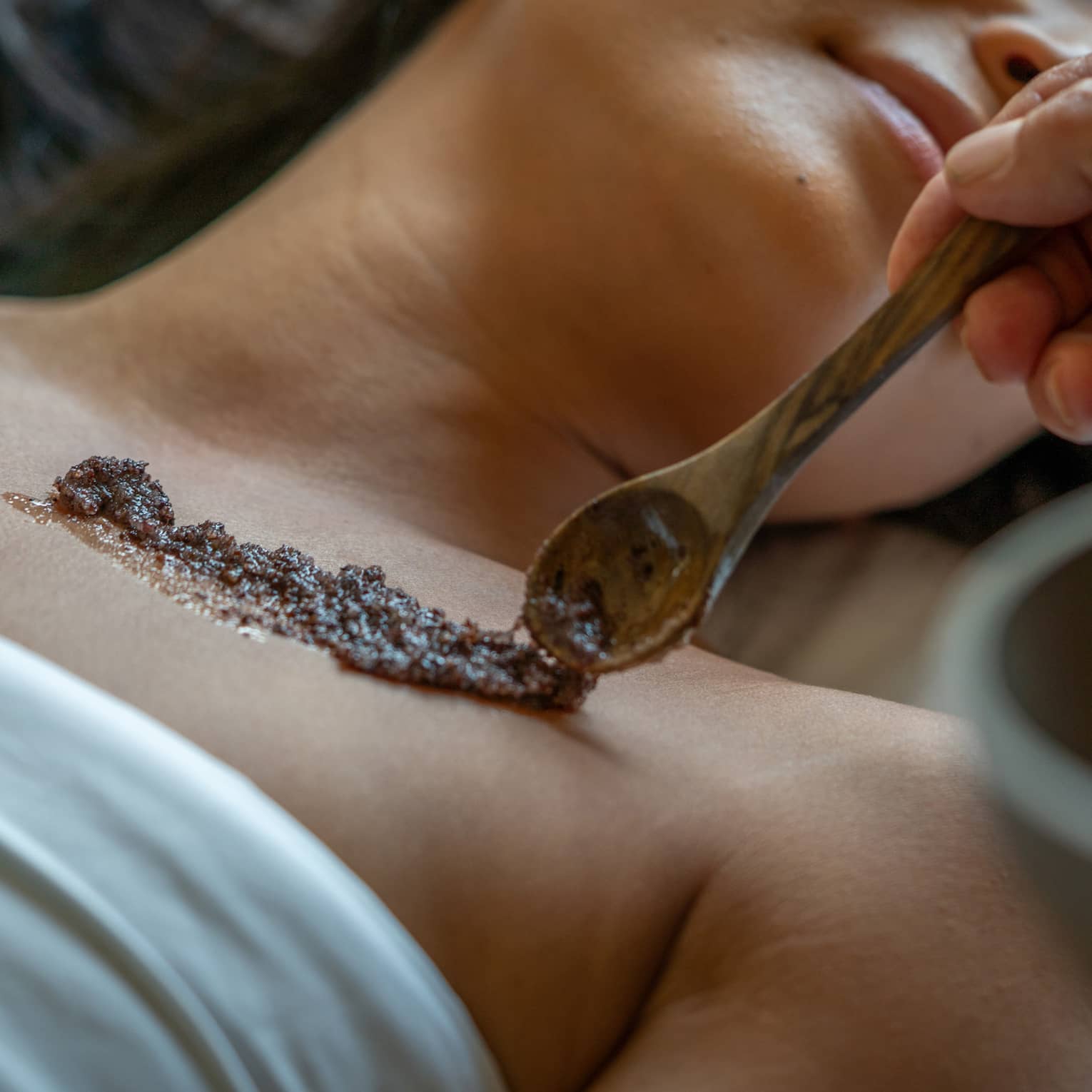 Person laying on a Spa bed while an exfoliating skin scrub is placed on their skin.