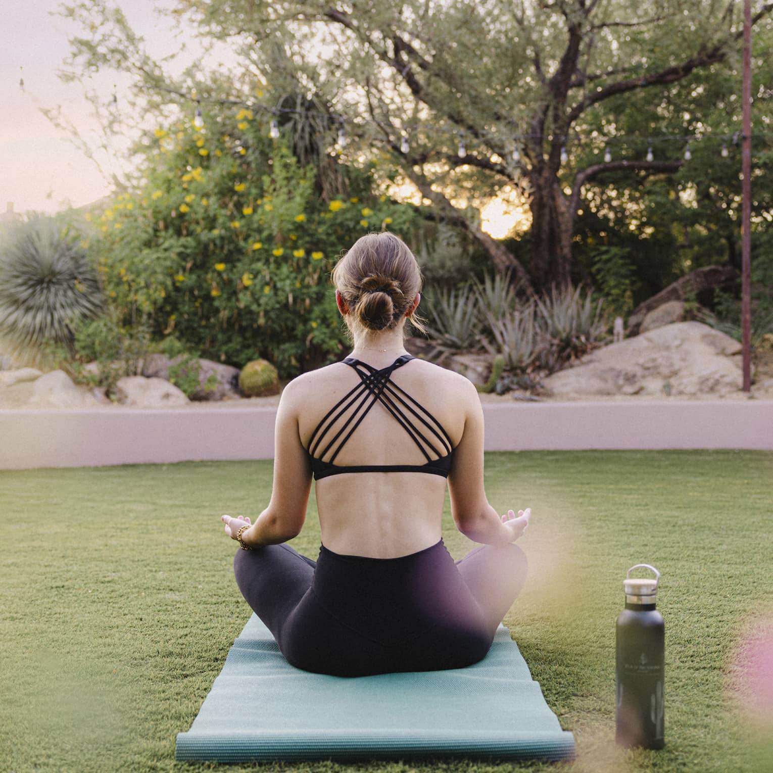 Person doing yoga outside on a blue yoga mat with a water bottle beside them.