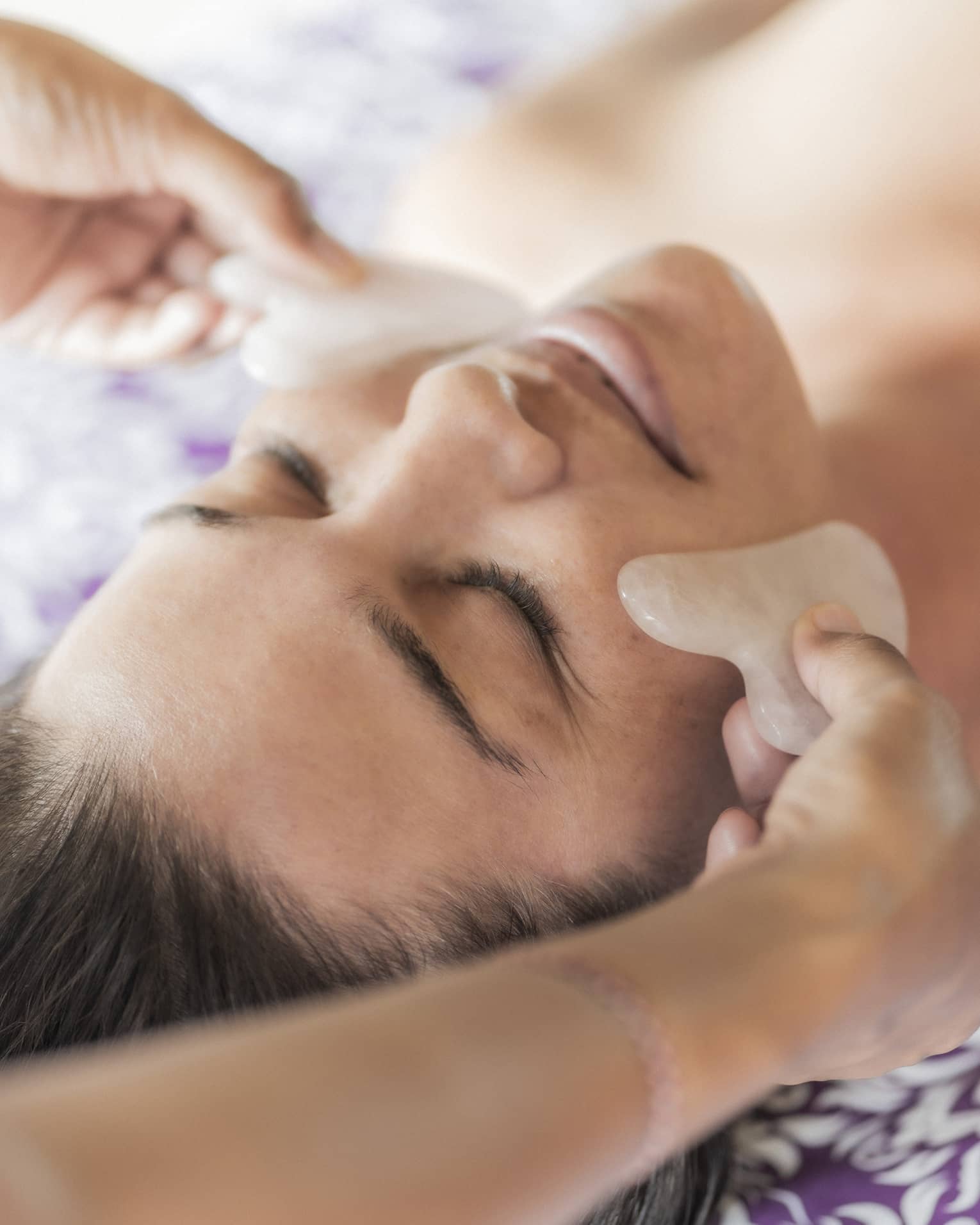 Hands hold stones at woman's cheeks on spa table