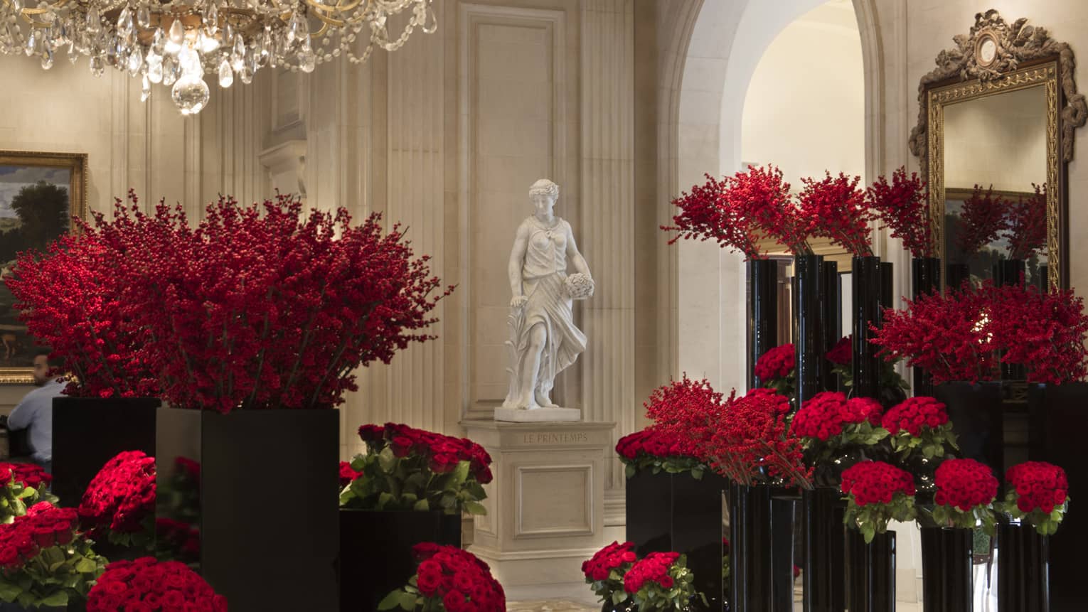 White statue in hotel lobby surrounded by tall black vases with red flowers