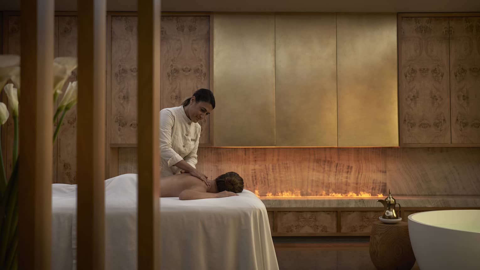 Person facedown on white spa table receiving massage from spa therapist