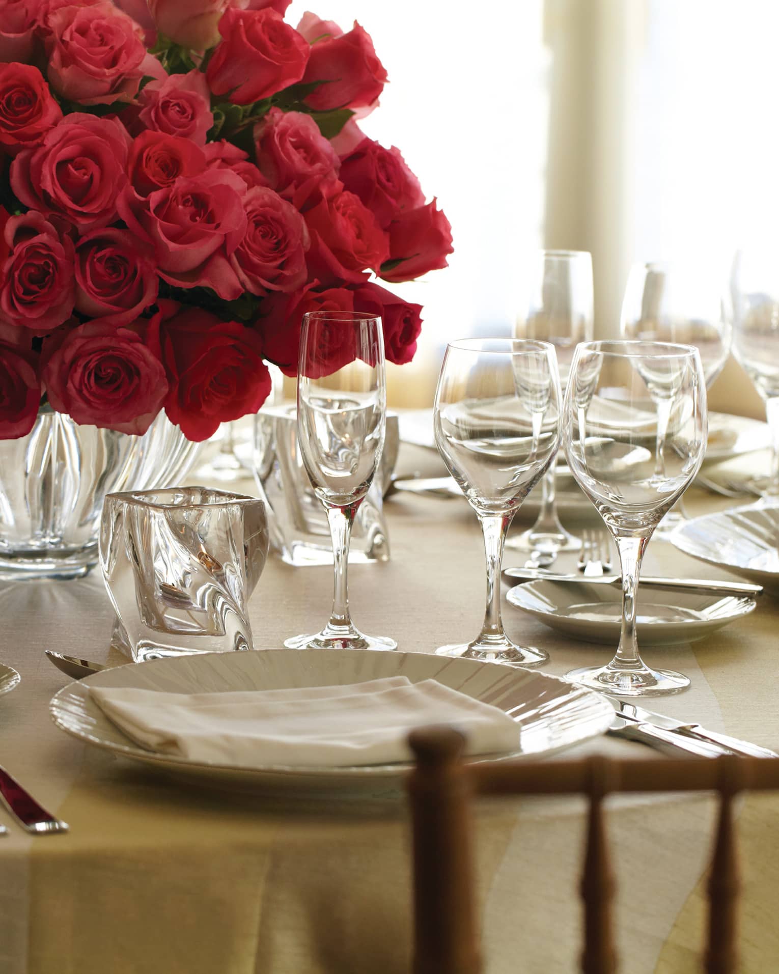 Banquet dining table place setting with plate, crystal glasses and vase with red rose bouquet