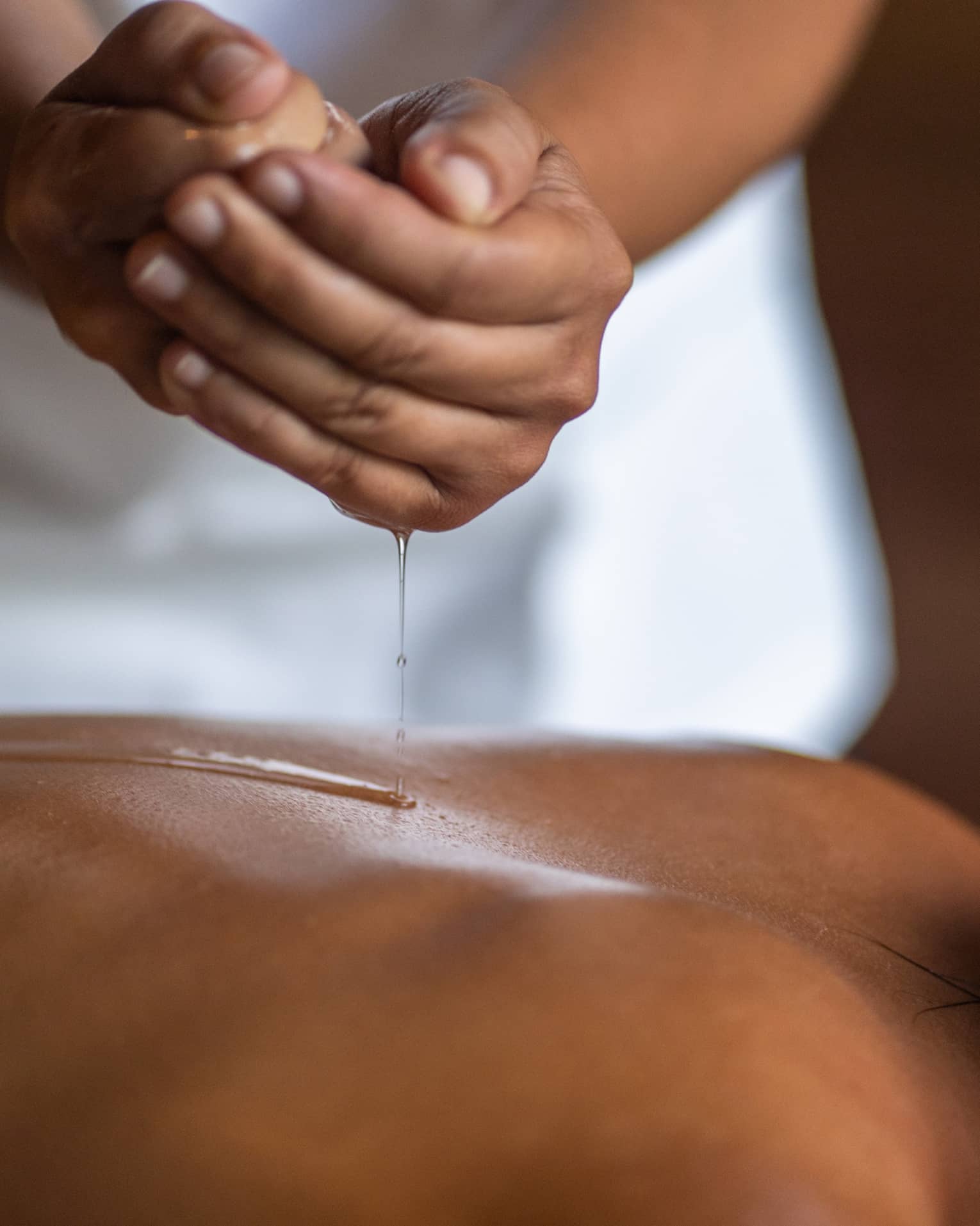 Delicate hands apply oil to a guest's back during a spa treatment