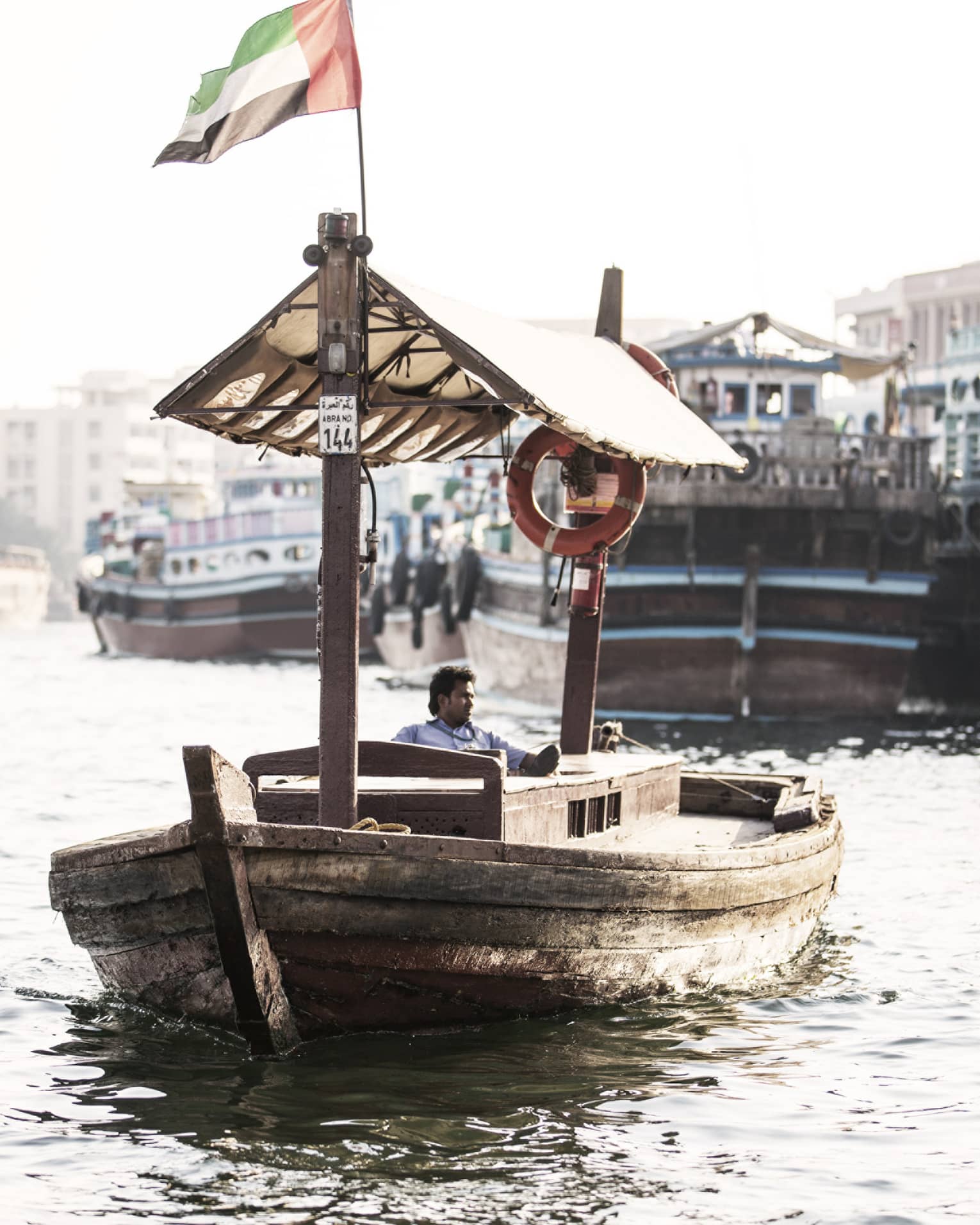 A small wooden boat flying the UAE flag as it sails down a small waterway.