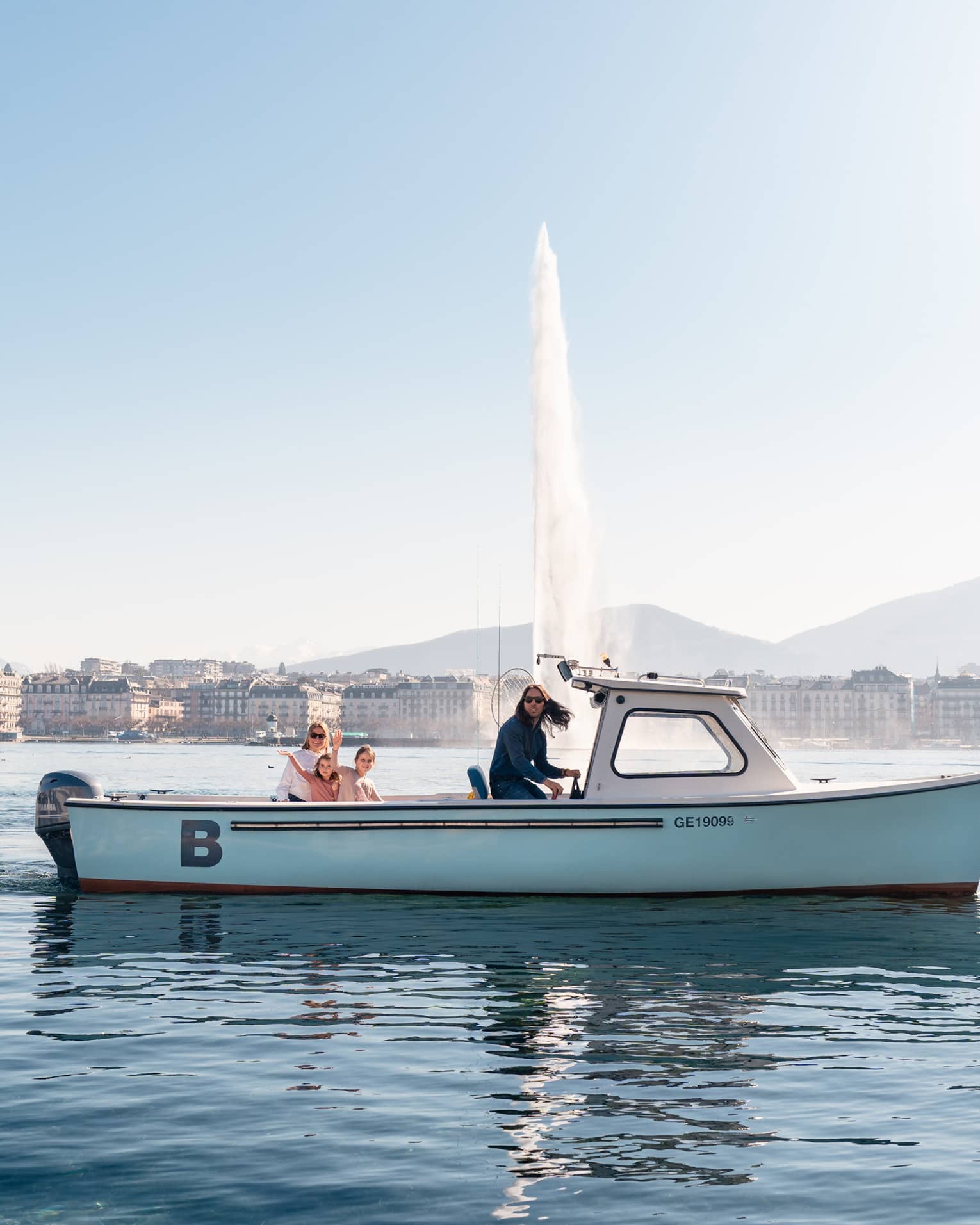 Four people in small boat on Lake Geneva with Jet d'Eau fountain and city in backdrop