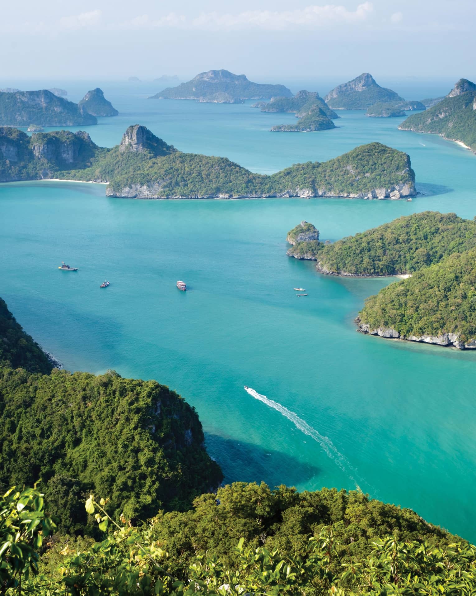 Aerial view of lush green mountains and islands, boats in blue ocean