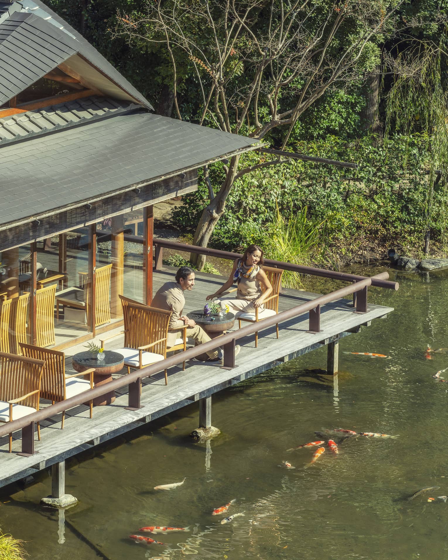 Two people sitting on an outdoor deck overlooking a pond with koi fish at Four Seasons