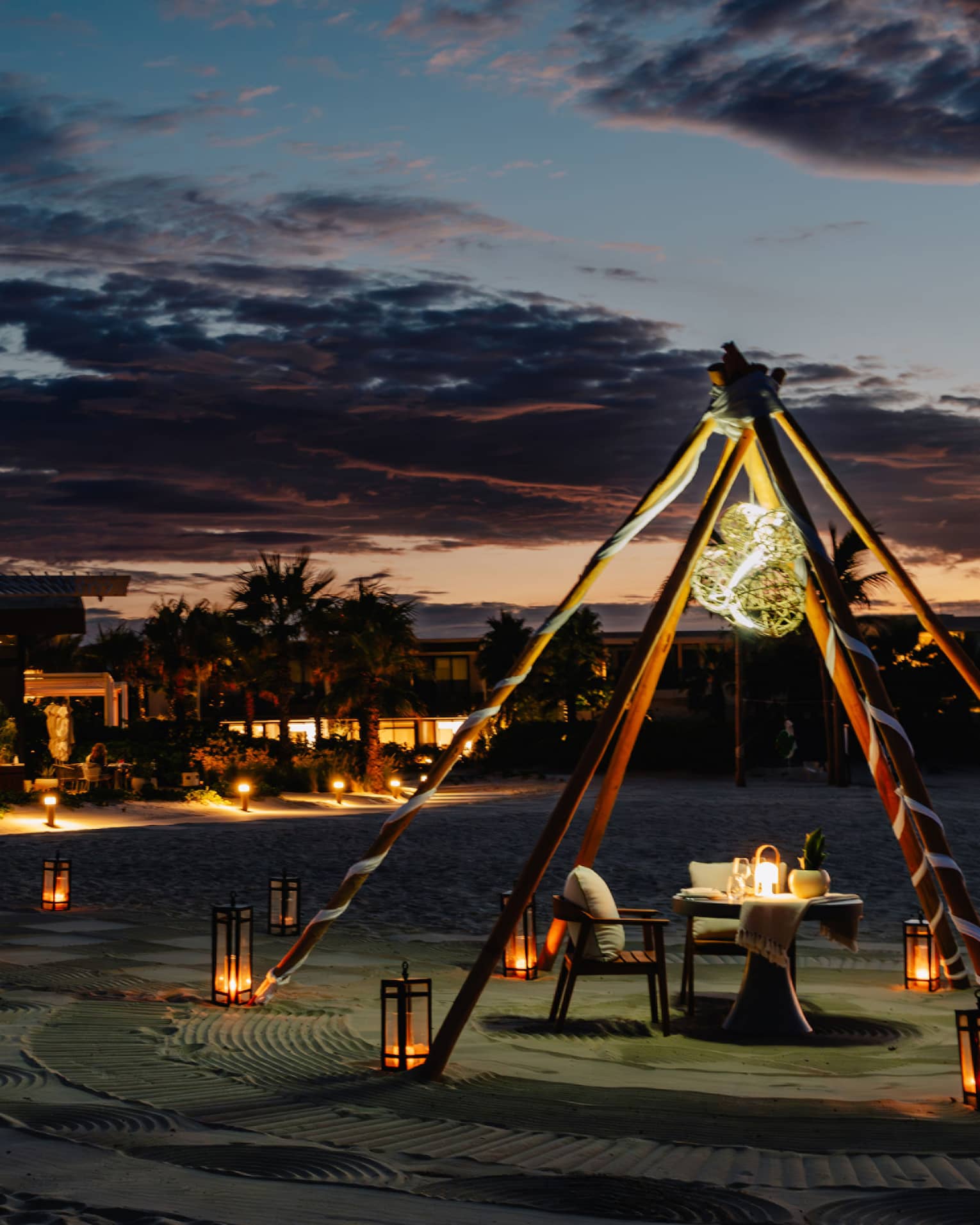 Outdoor tent with a chair and dining table, surrounded by lanterns on the ground in the evening.