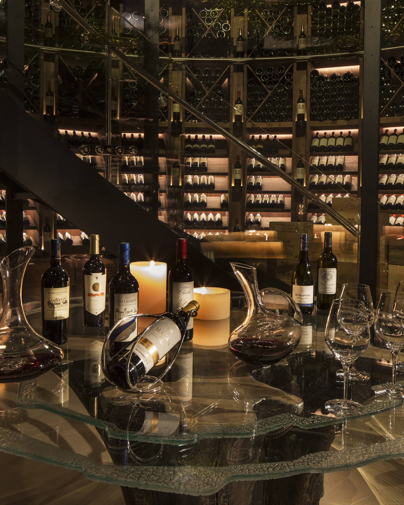 Bottles of wine are arranged for a tasting within an expansive, candlelit wine cellar