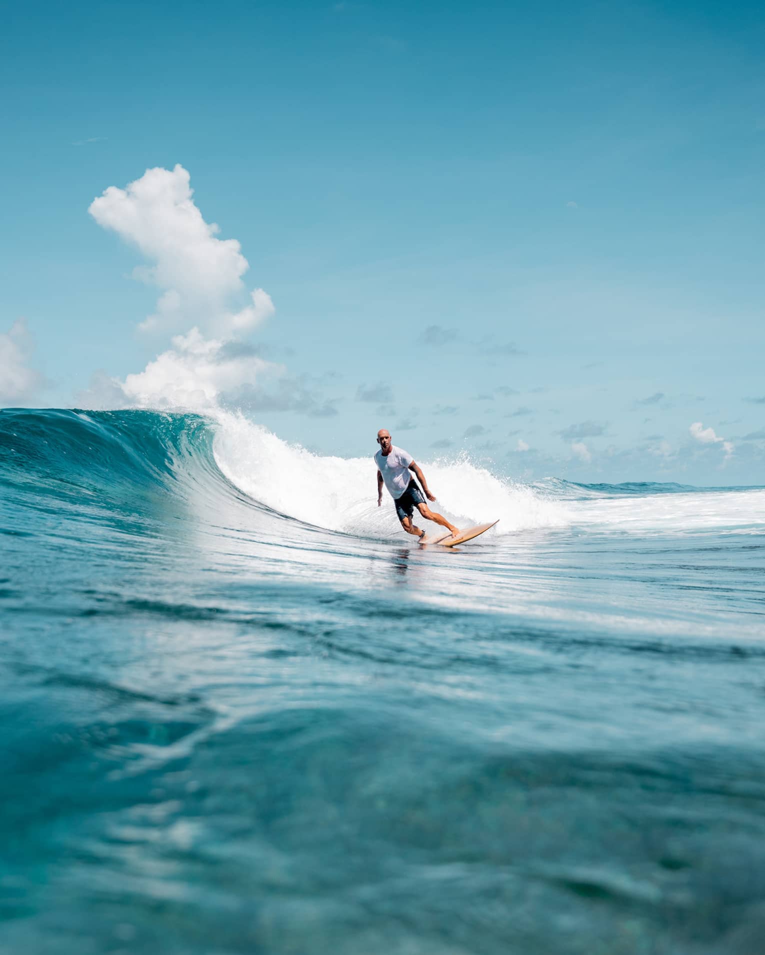 A person surfing a wave in the ocean, the water is a deep blue matched by the blue sky.