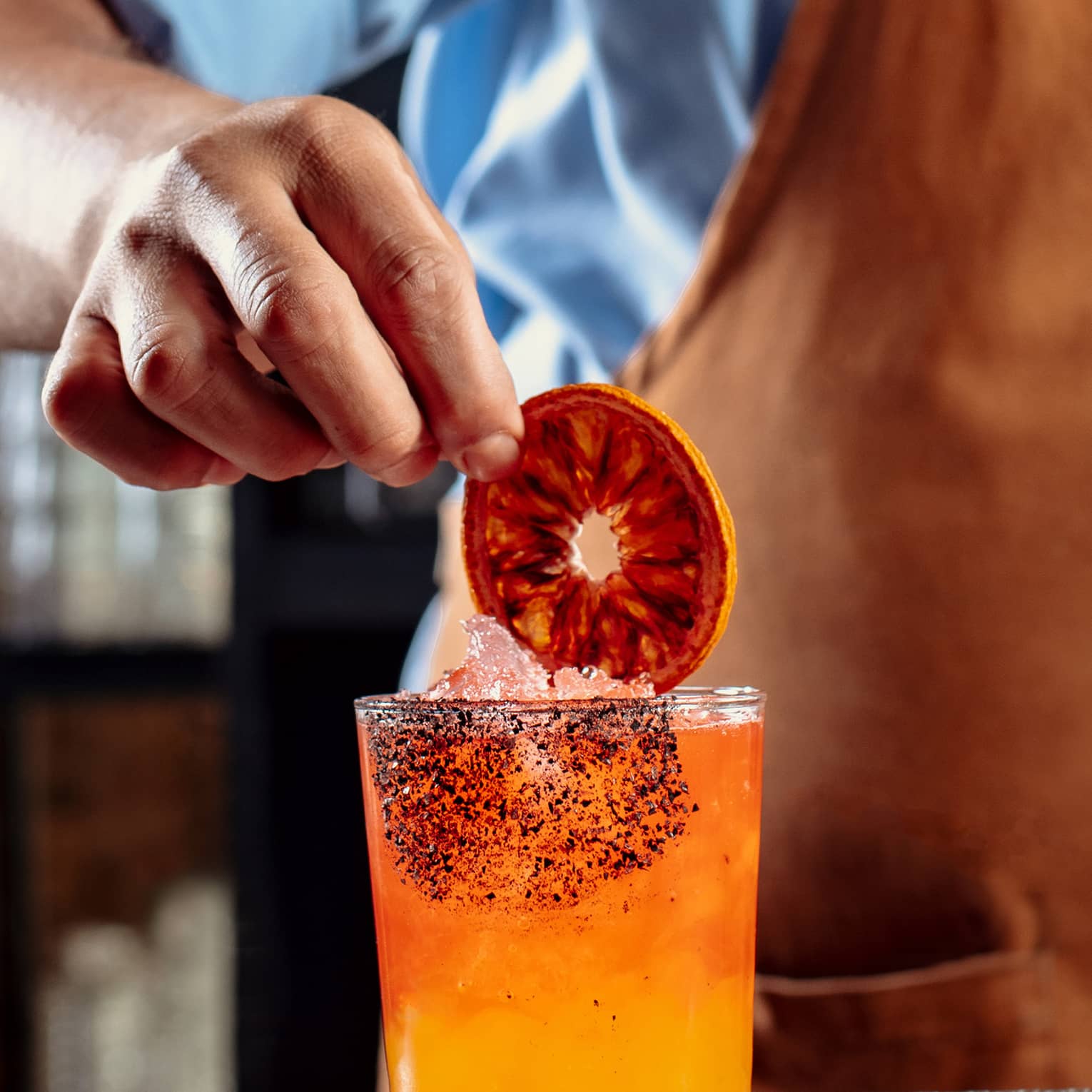 A bartender making an orange cocktail and putting a dark orange wheel in it.