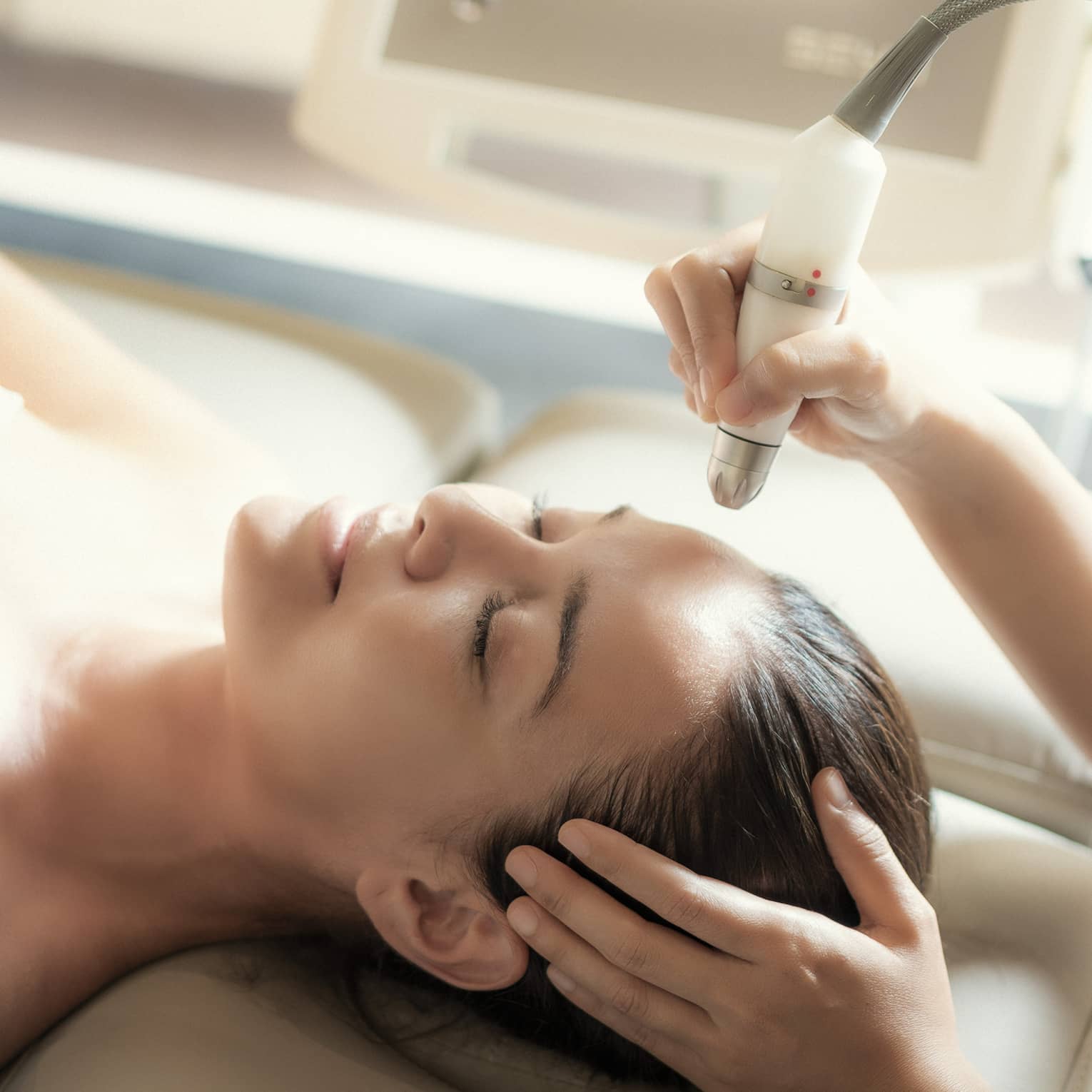 An aesthetician uses a tool on the face of a relaxing woman.