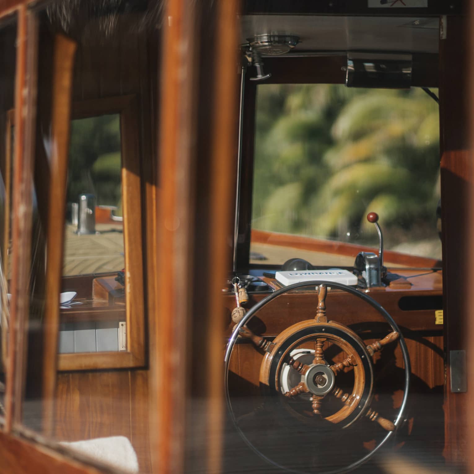View from outside into a boat's cockpit cabin, both the boat's frame and the wheel partly made of rustic deep-brown wood.