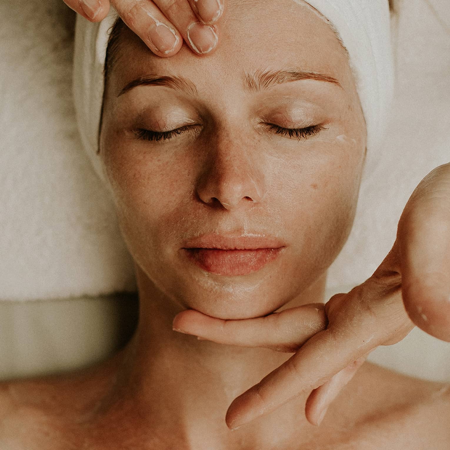 Person receiving a relaxing facial massage with eyes closed and head wrapped in a towel
