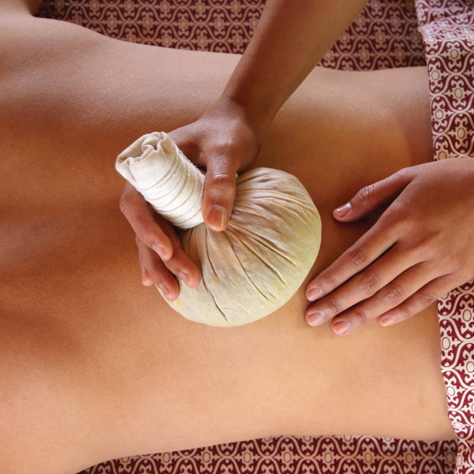 Masseuse rubs herbal sac on woman's bare back in spa