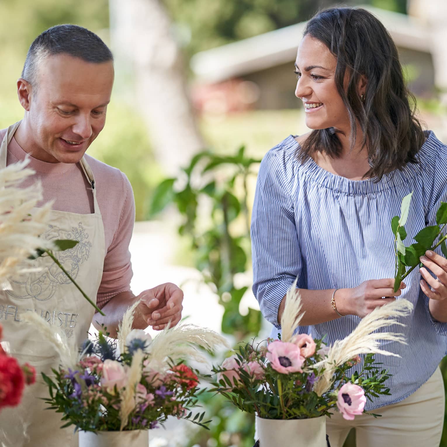 Two people stand outside at a table putting together floral bouquets