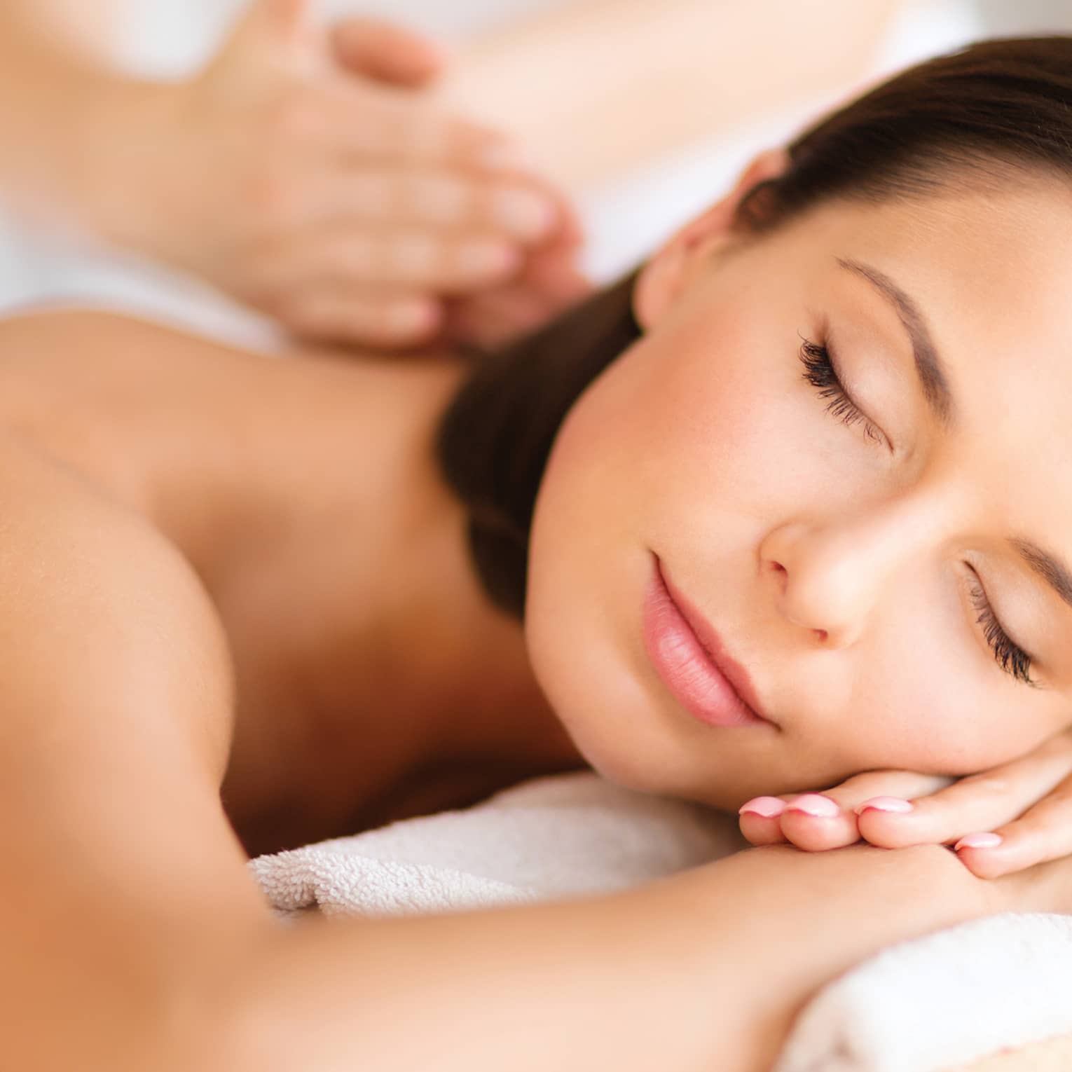 Woman lies on massage table, closes eyes. rests head on arms as spa staff massages back