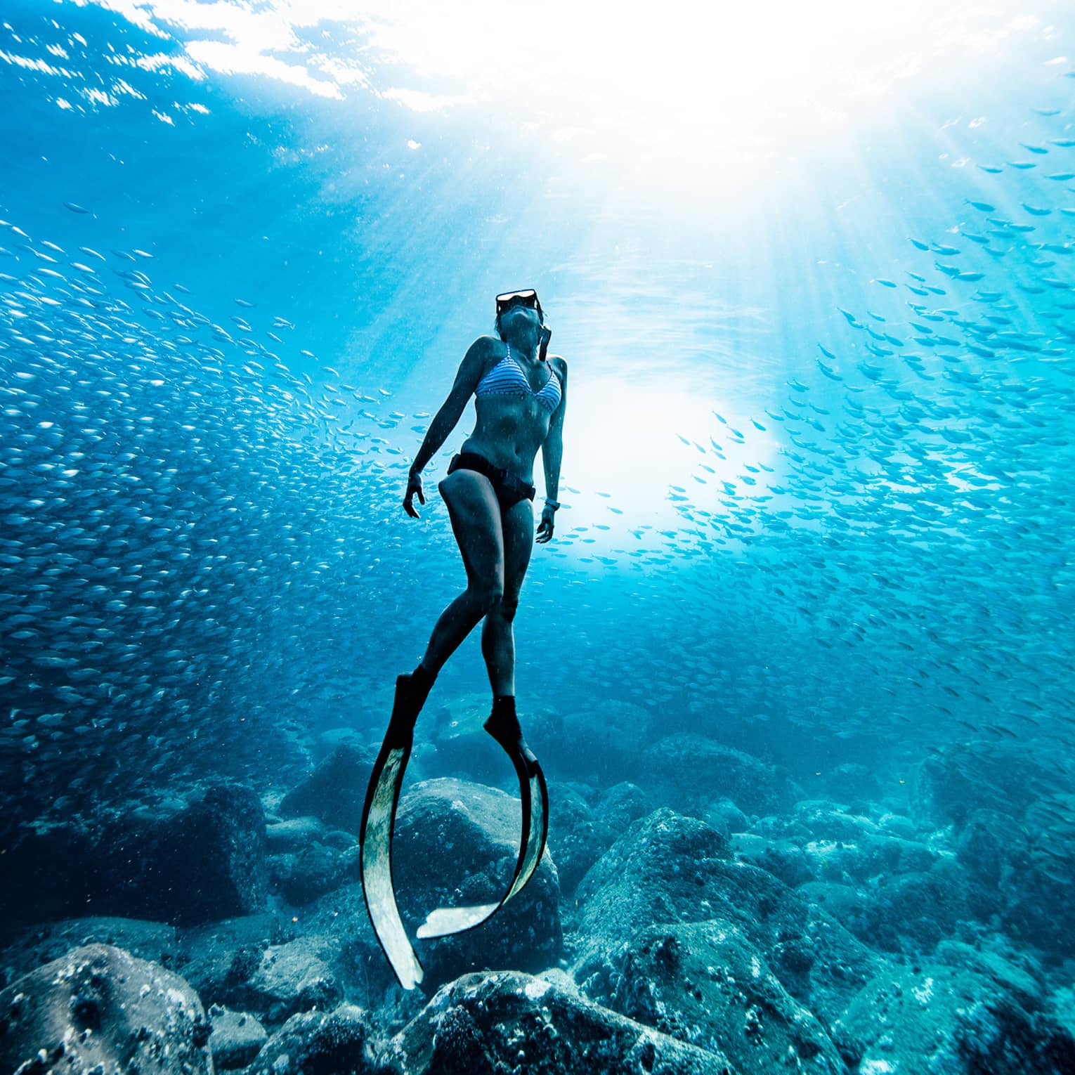 A woman in bikini wears scuba slippers below the surface of the ocean water