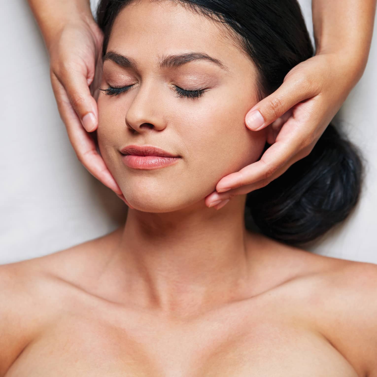 Woman with eyes closed as hands massage her face