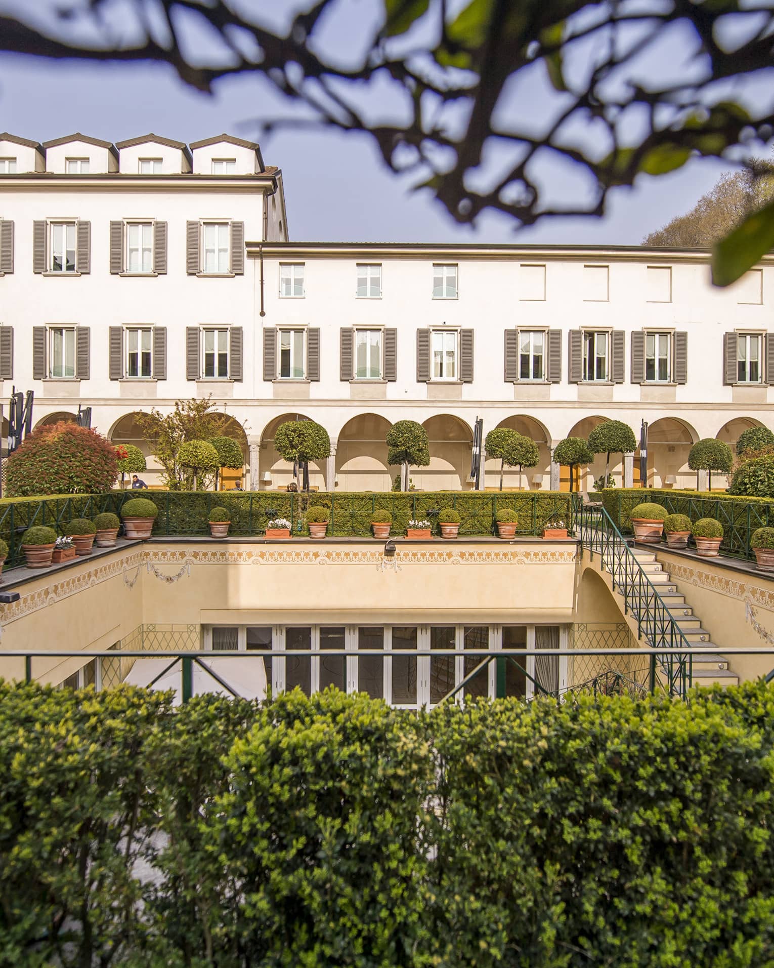 Shrubs, potted plants around rectangular courtyard garden under Four Seasons Hotel Milan building