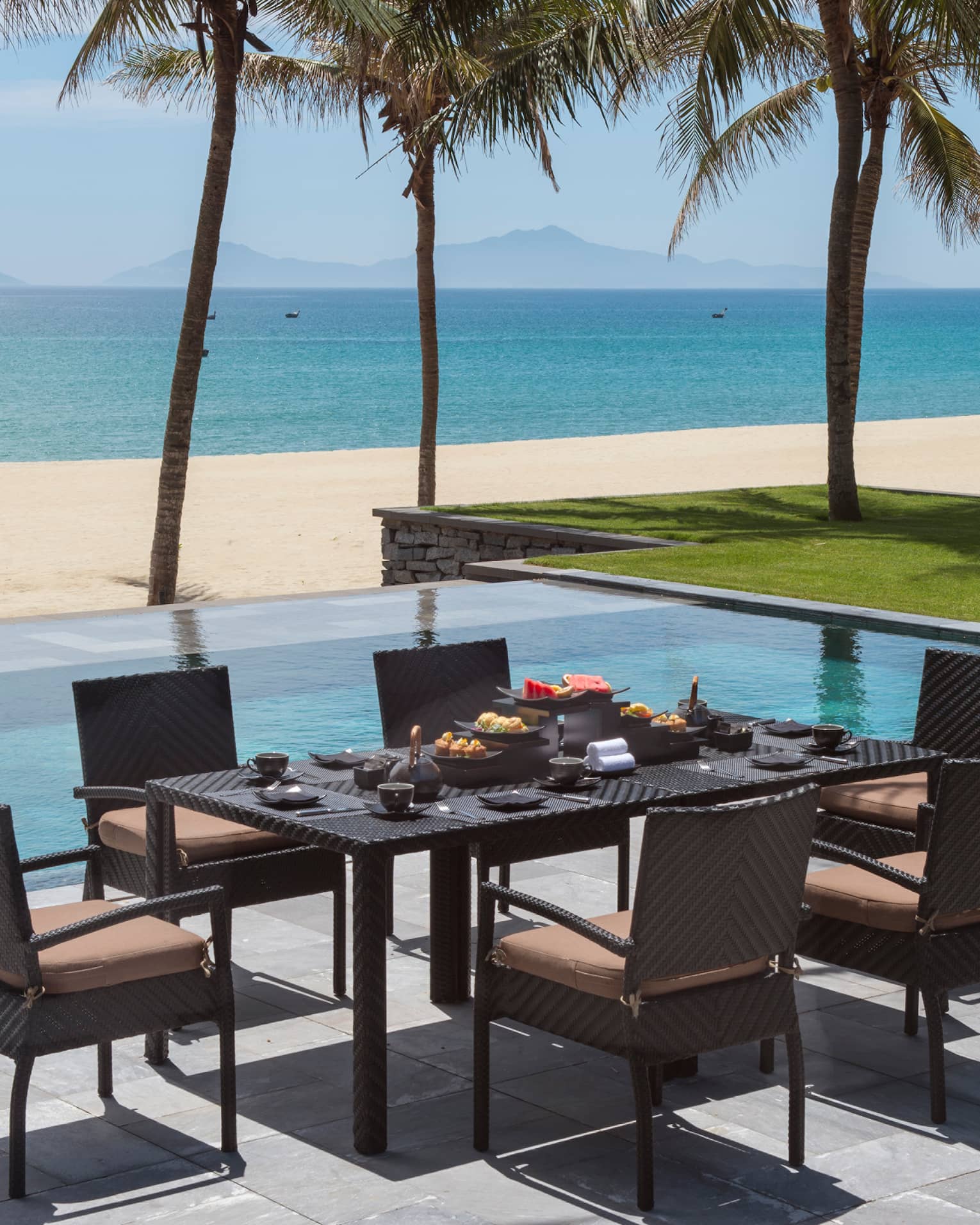 Villa dining table on stone patio by outdoor swimming pool