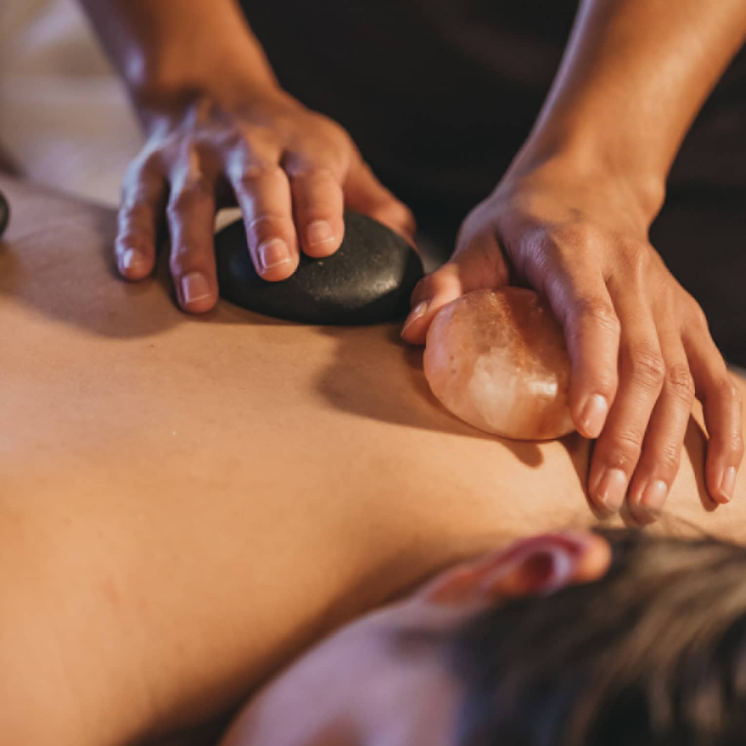 Close up of hands massaging warm stones on a woman's bare back