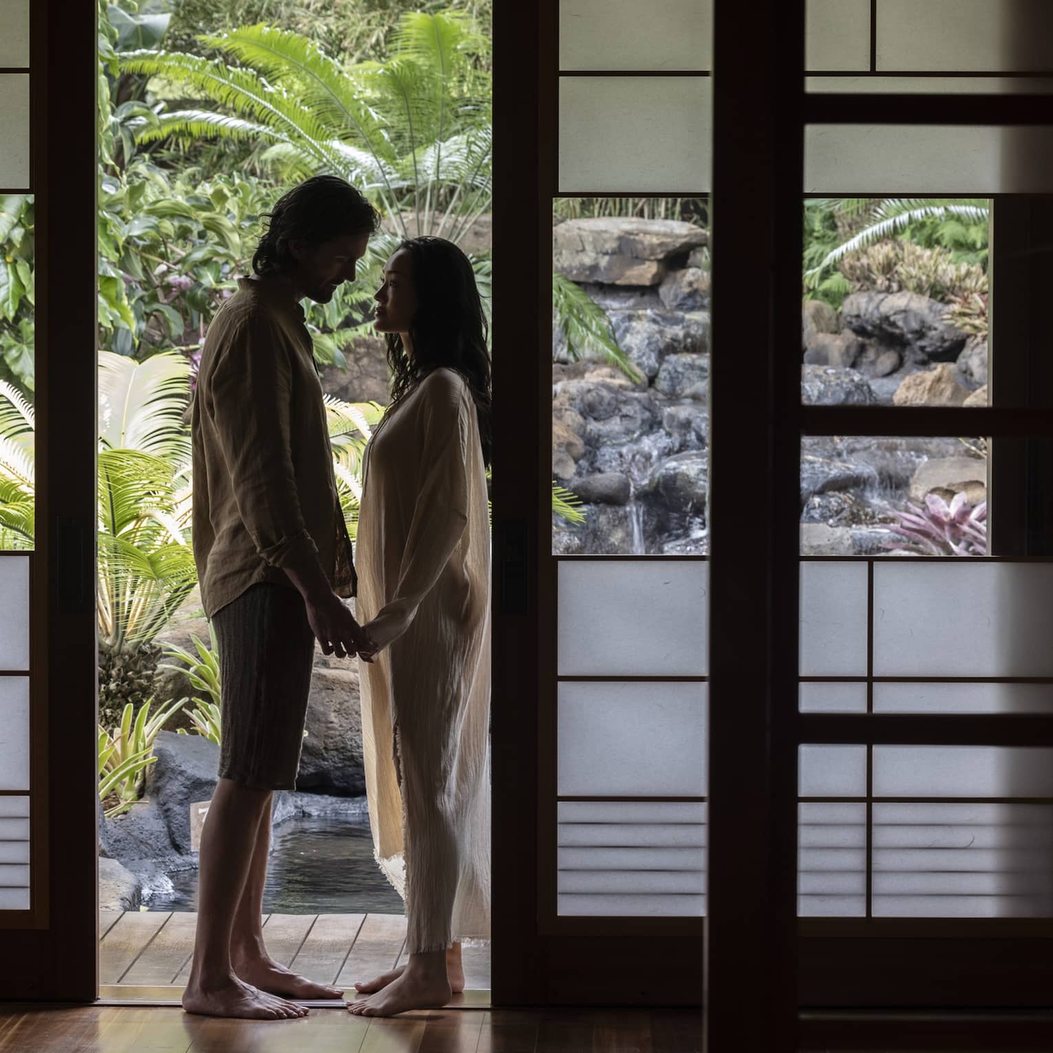 Man and woman stand holding hands in doorway of private spa hale at Sensei Lanai, A Four Seasons Resort