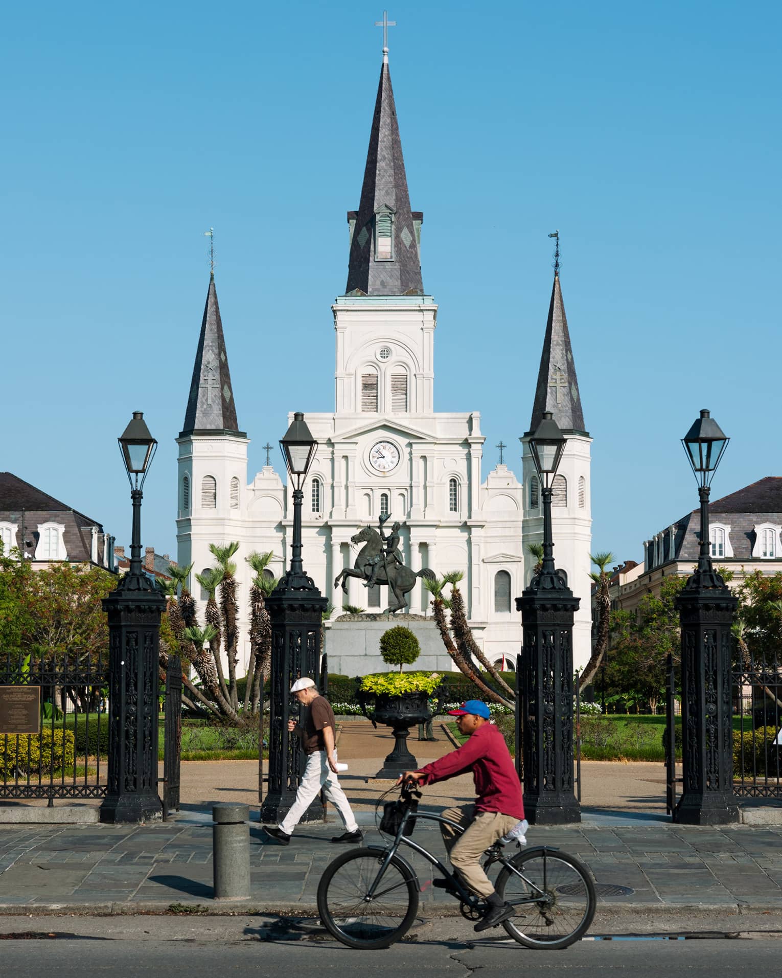 A person riding a bike in front of a large gated building.