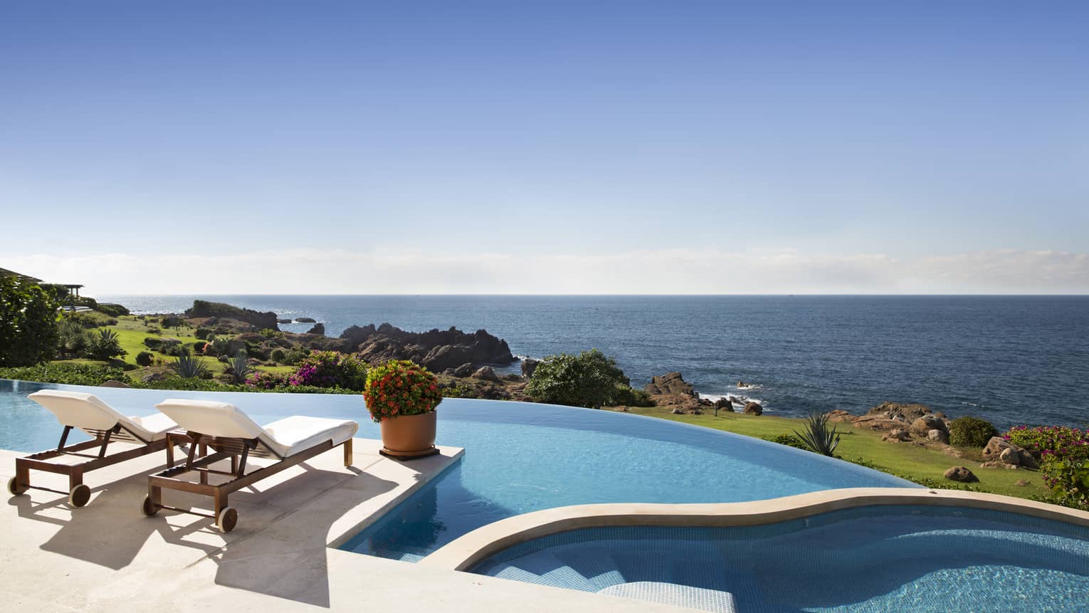 An outdoor terrace at an oceanfront villa in mexco with two lounge chairs and large infinity pool, with expansive sea views.