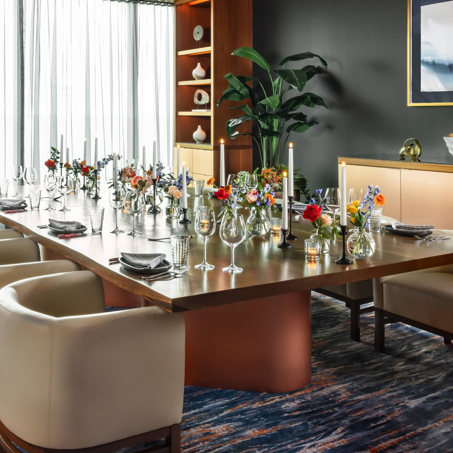 Dining table set with glasses and vases of flowers in a room with floor-to-ceiling windows