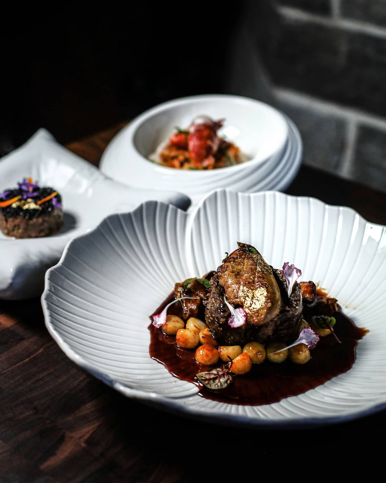 Three white plates of food set on a dark table with a dark backdrop
