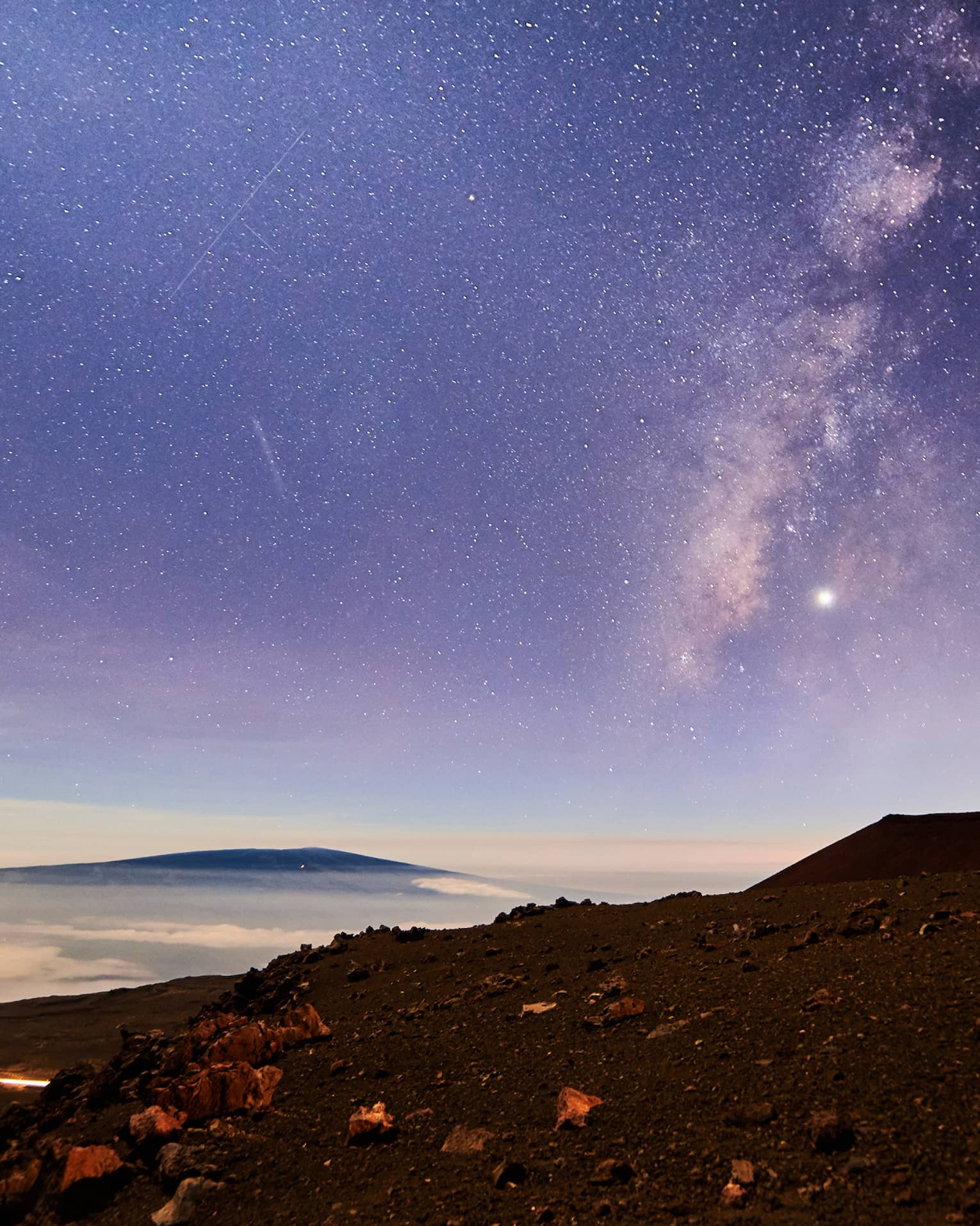 Sunrise under starry sky above mountain, volcanic rocks