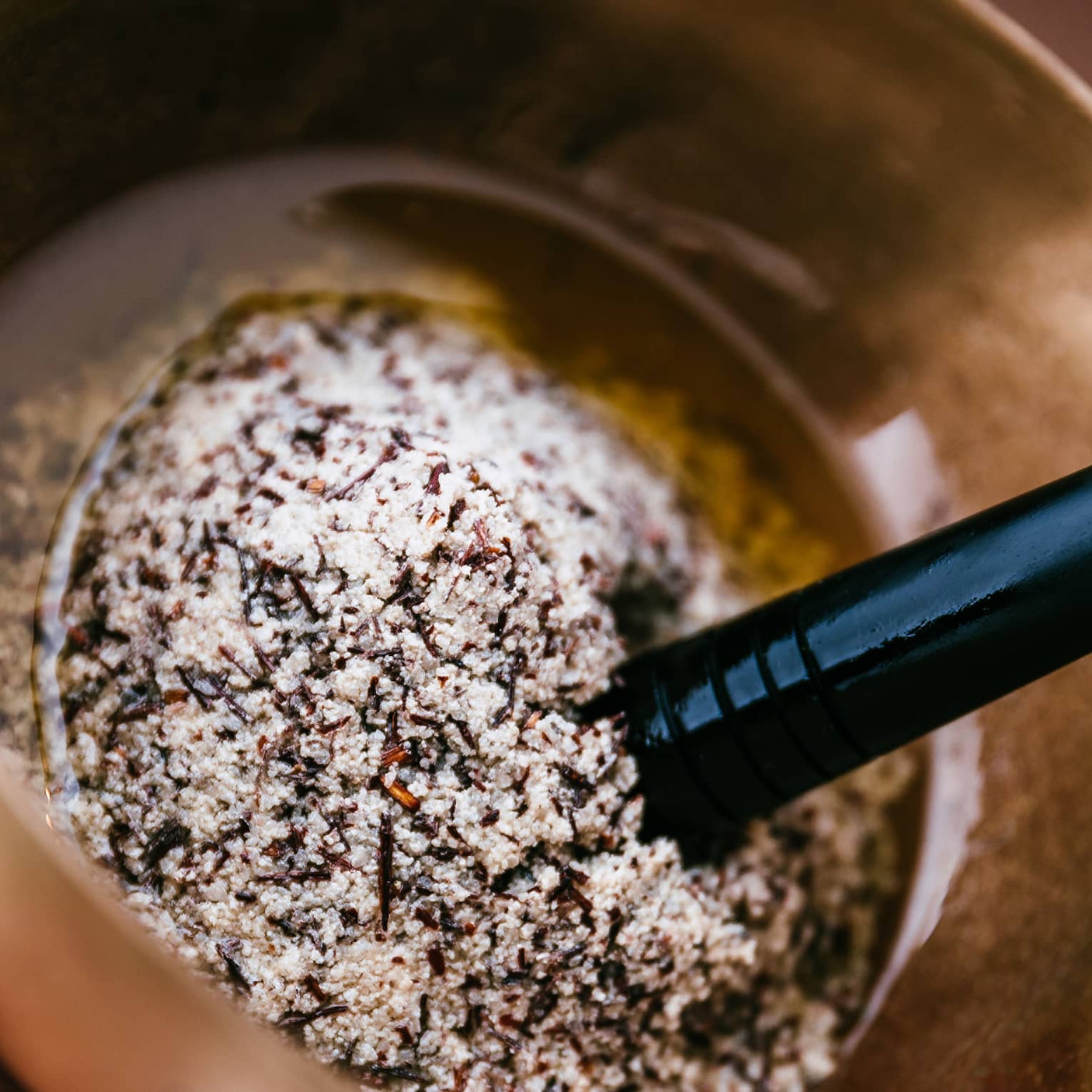 A person uses a golden mortar and pestle to grind several salts and spices into oil.