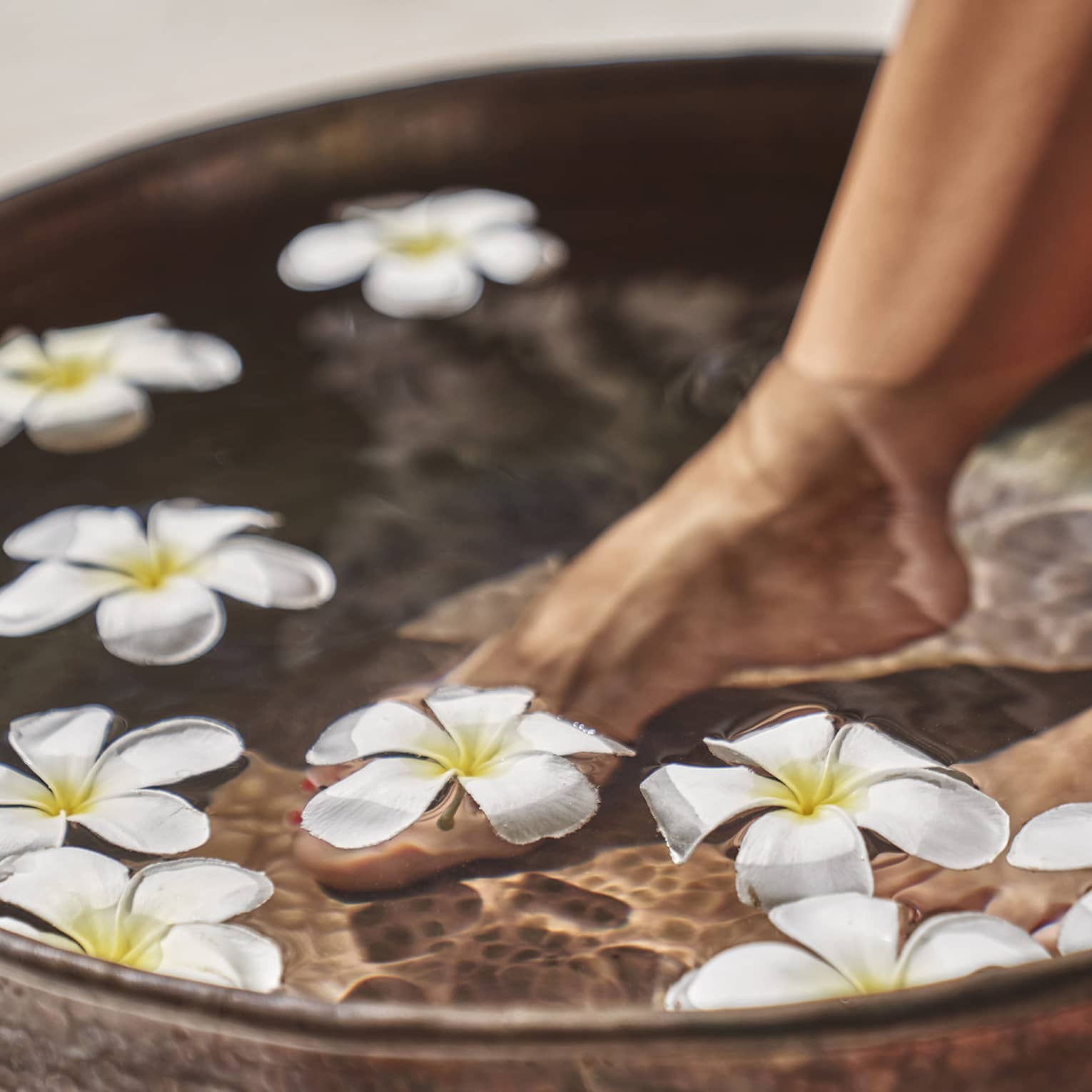 A woman's feet in a bowl of water and flowers.