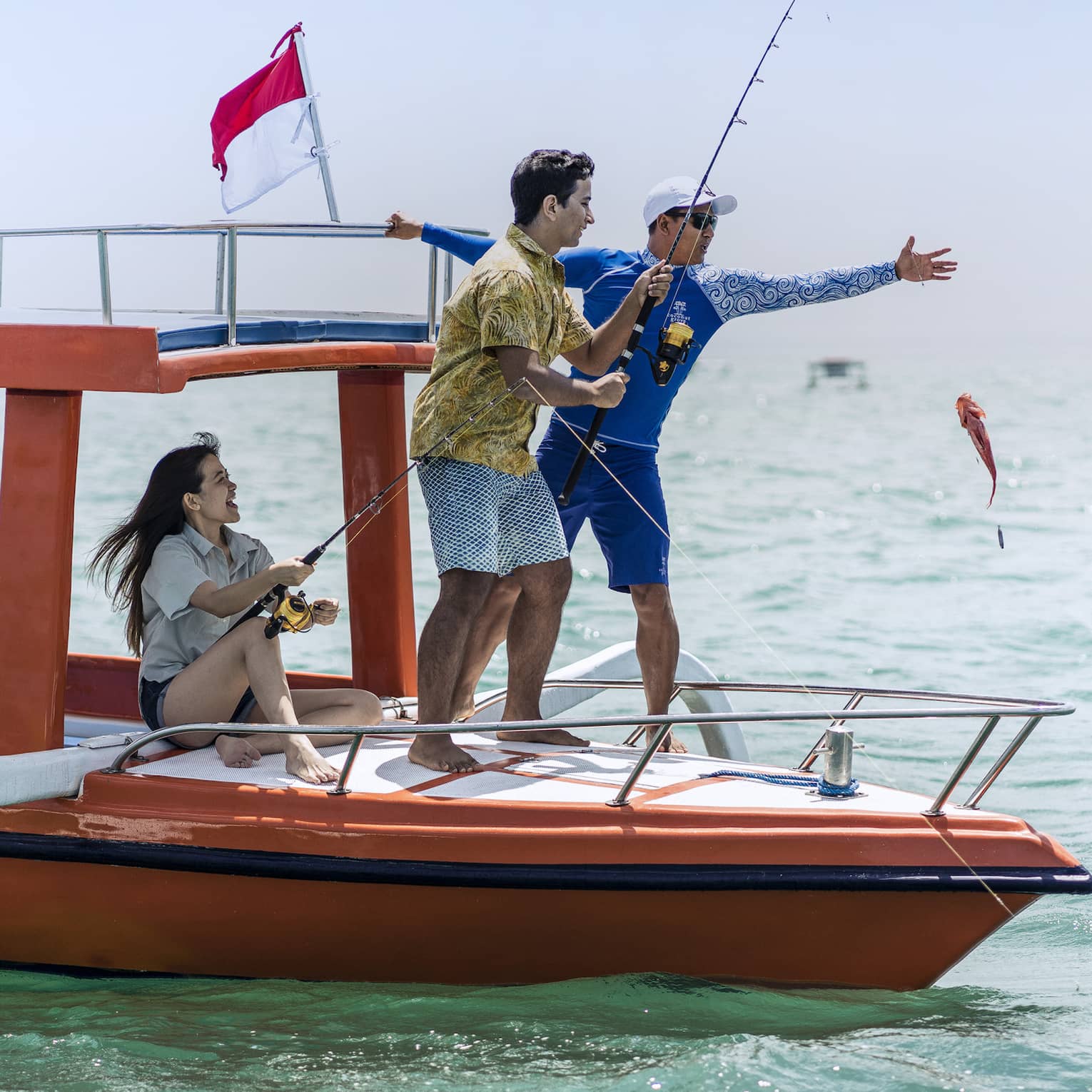 Tour guide teaches two guests to fish on a traditional jukung fishing boat on the open ocean