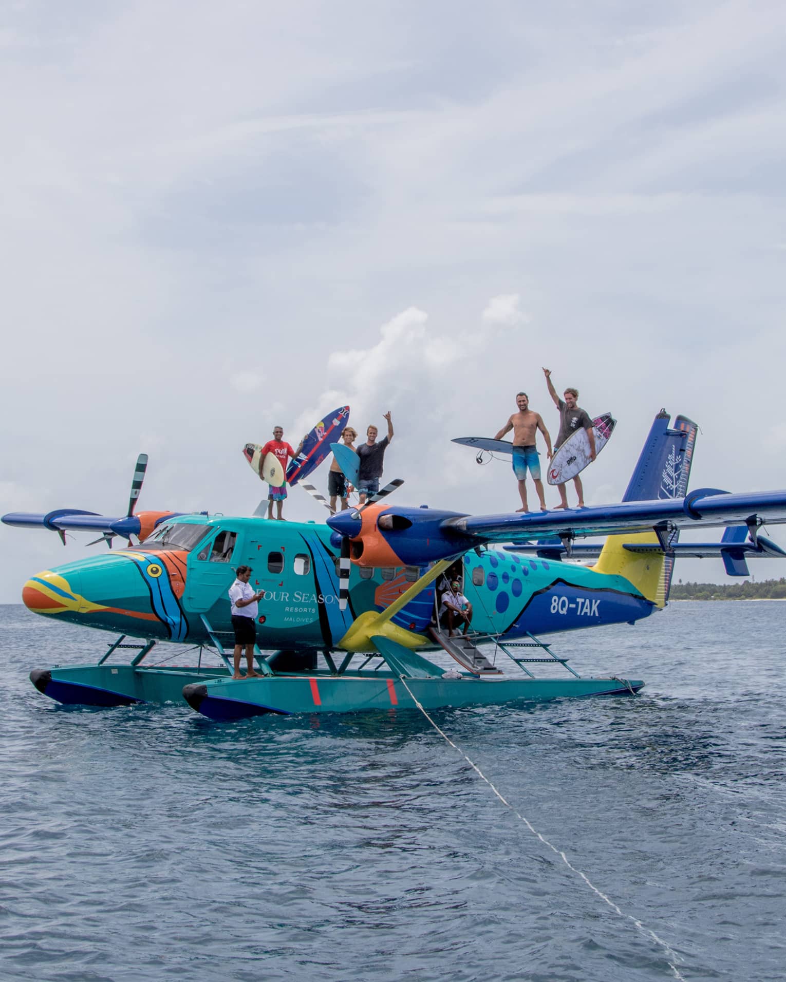 A group of people standing on top of a seaplane holding surfboards out on the water