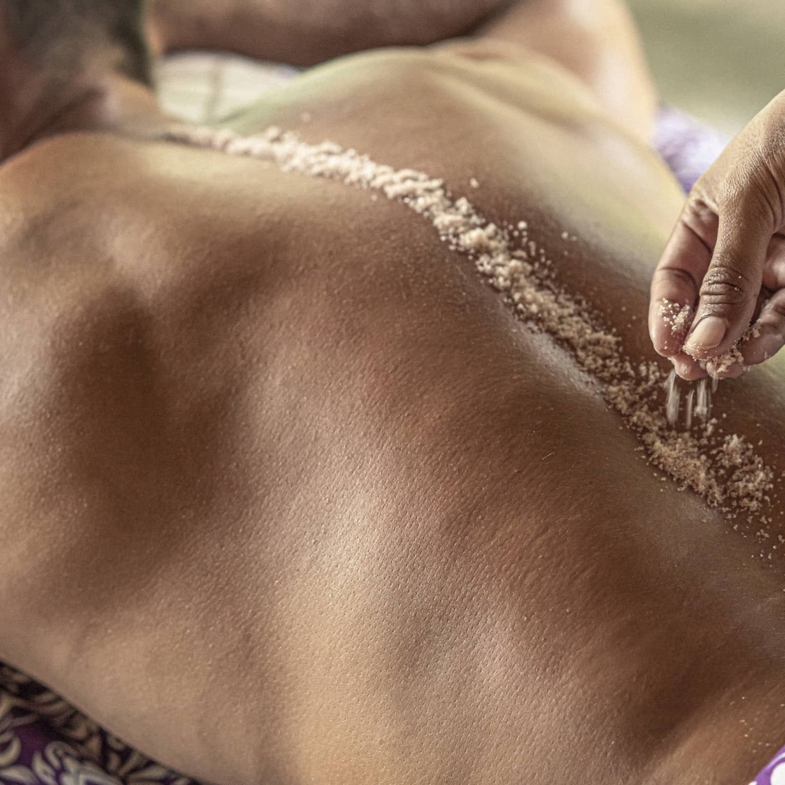 Hand place spa salts along man's spice during Sacred River Spa Massage