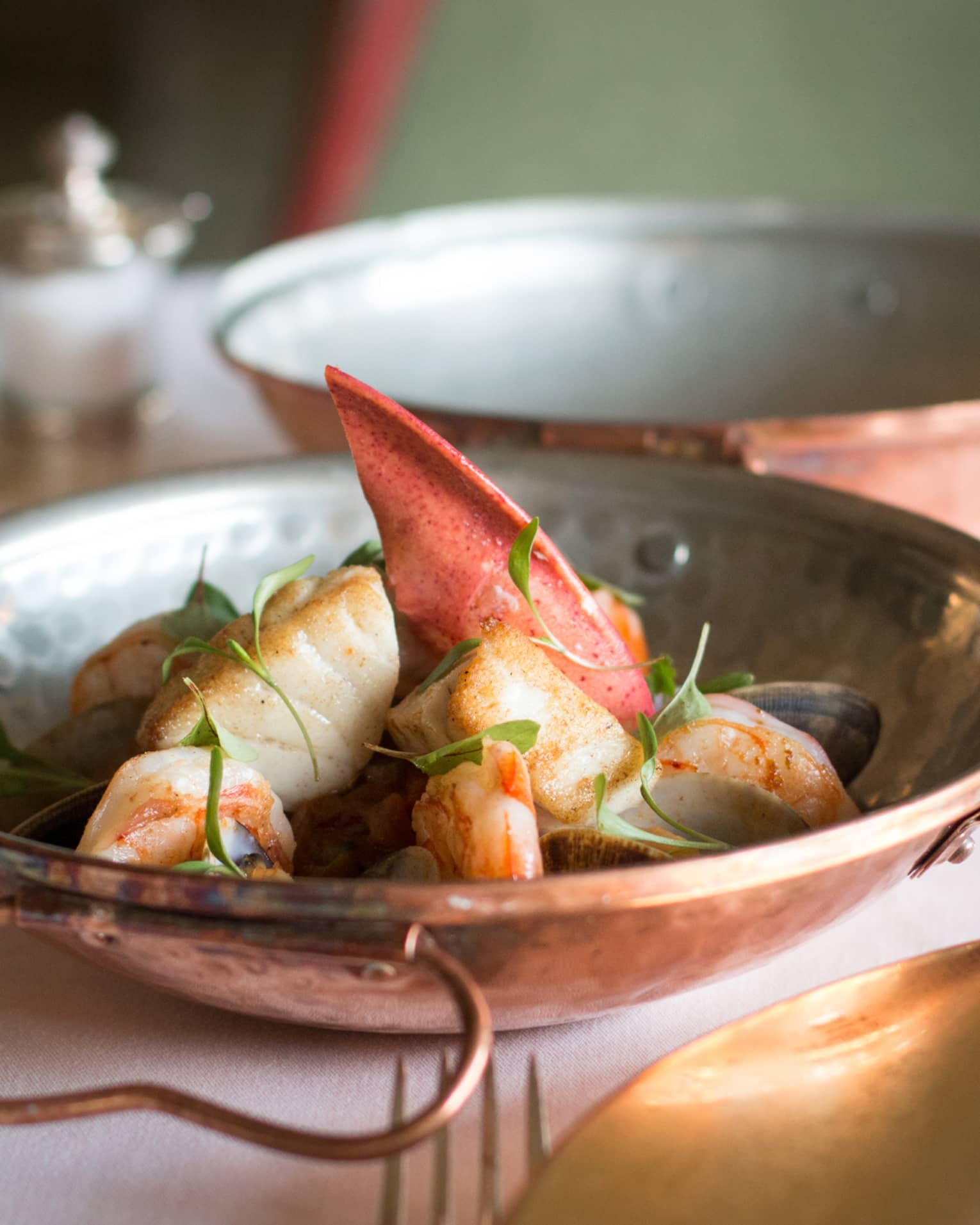 Close-up of copper bowl on table with lobster claw meat, seafood, green herb garnish