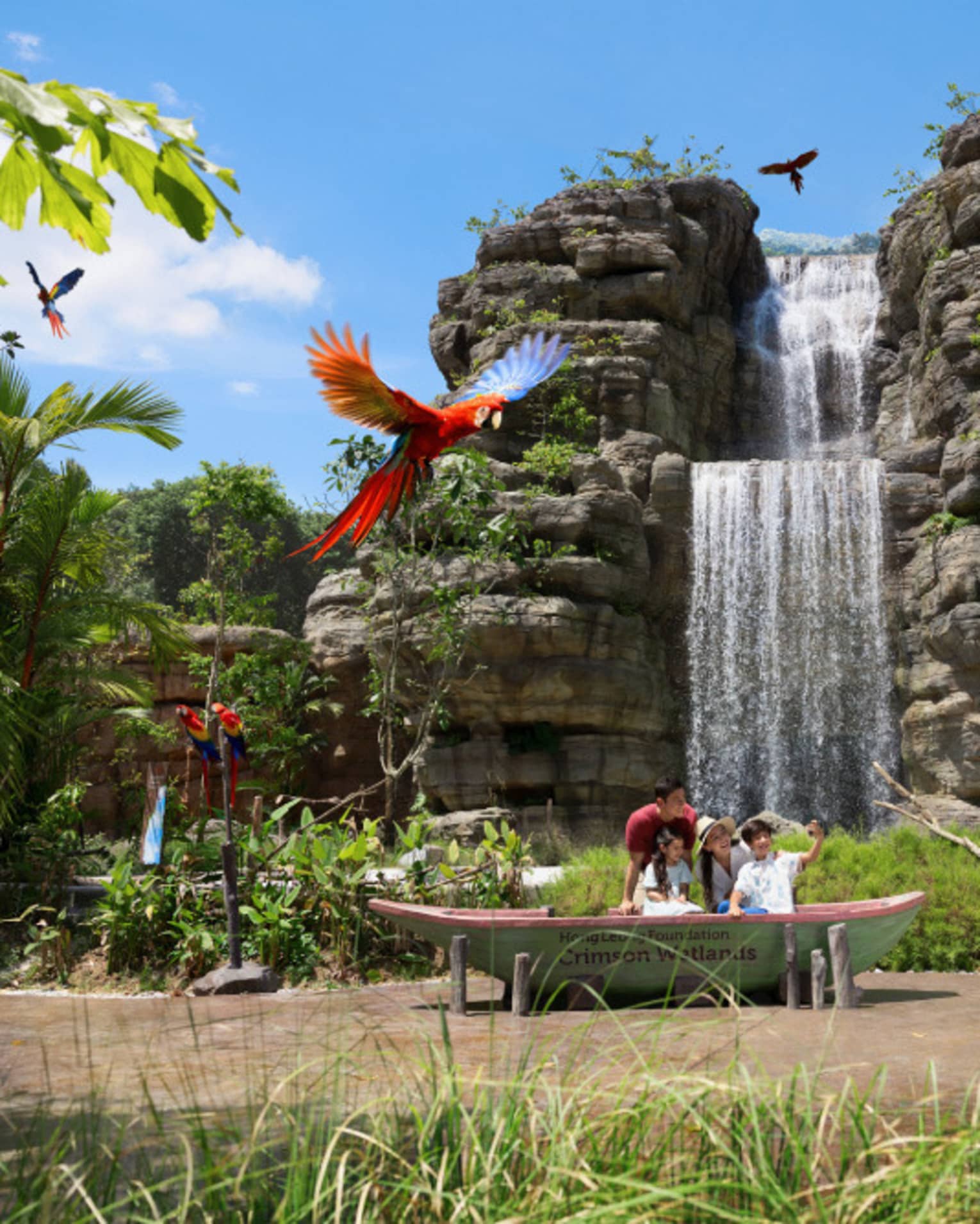 In front of a tall waterfall and stone formation, a family of four looks skyward at a flock of flying multi-coloured parrots.