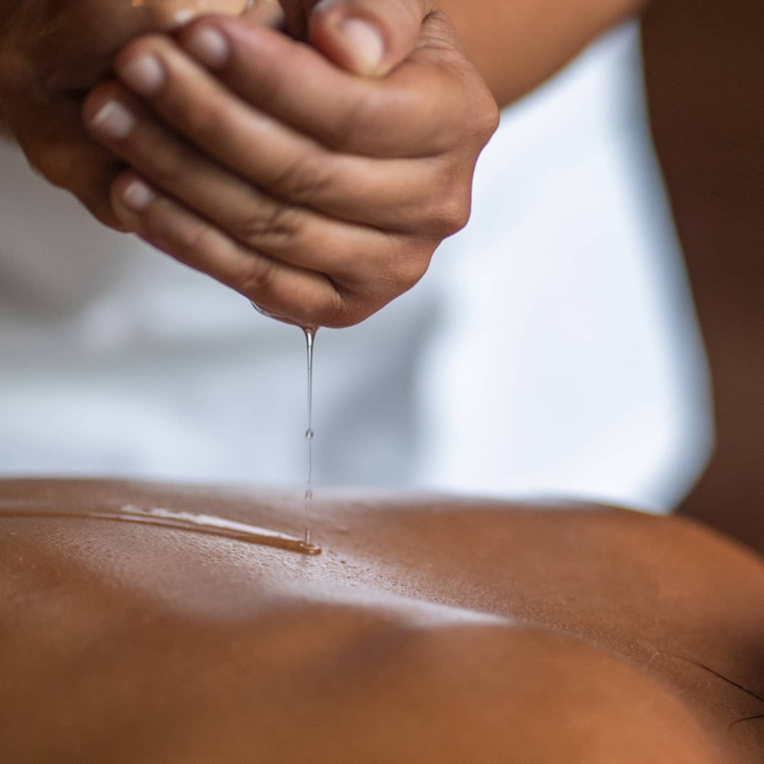 Delicate hands apply oil to a guest's back during a spa treatment