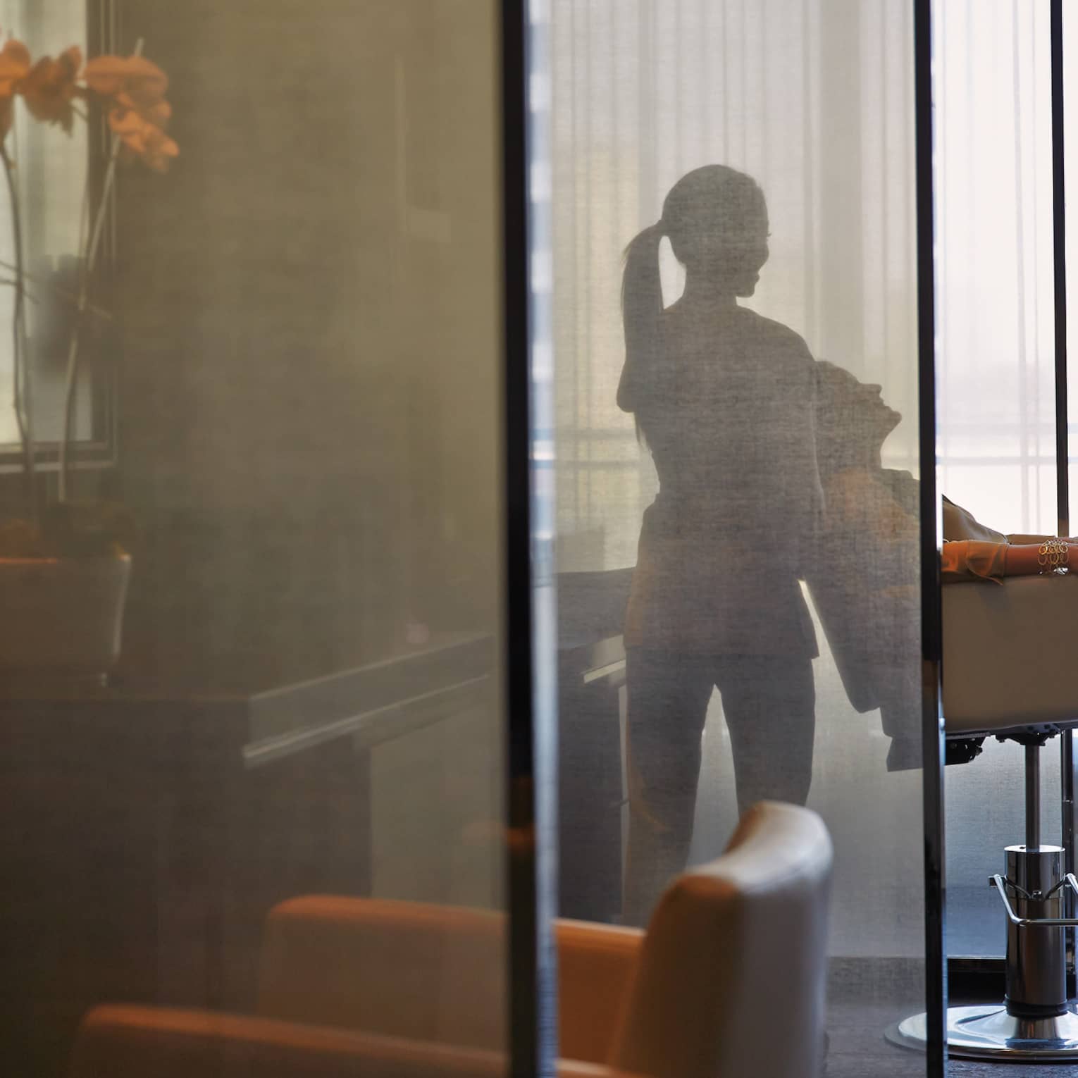 Silhouette of spa staff tilting woman back in salon chair behind sheer screen