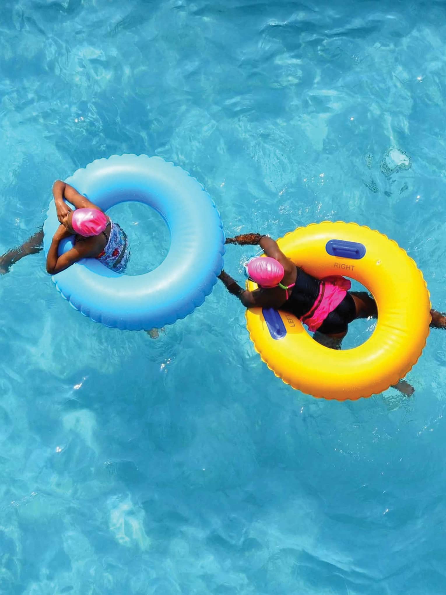 Aerial view of two swimmers in pink caps floating in blue and yellow inner tubes