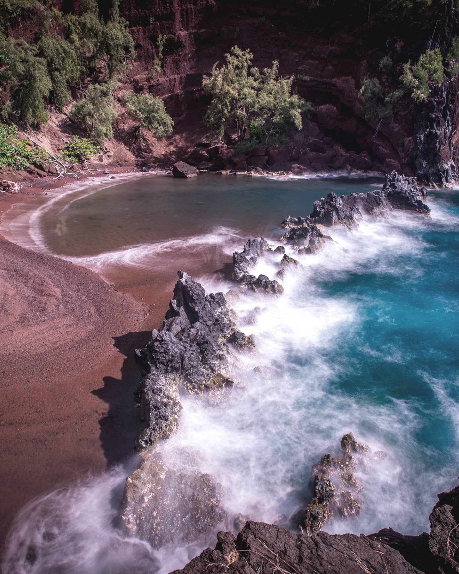 A red sand beach with waves crashing onto the sand.
