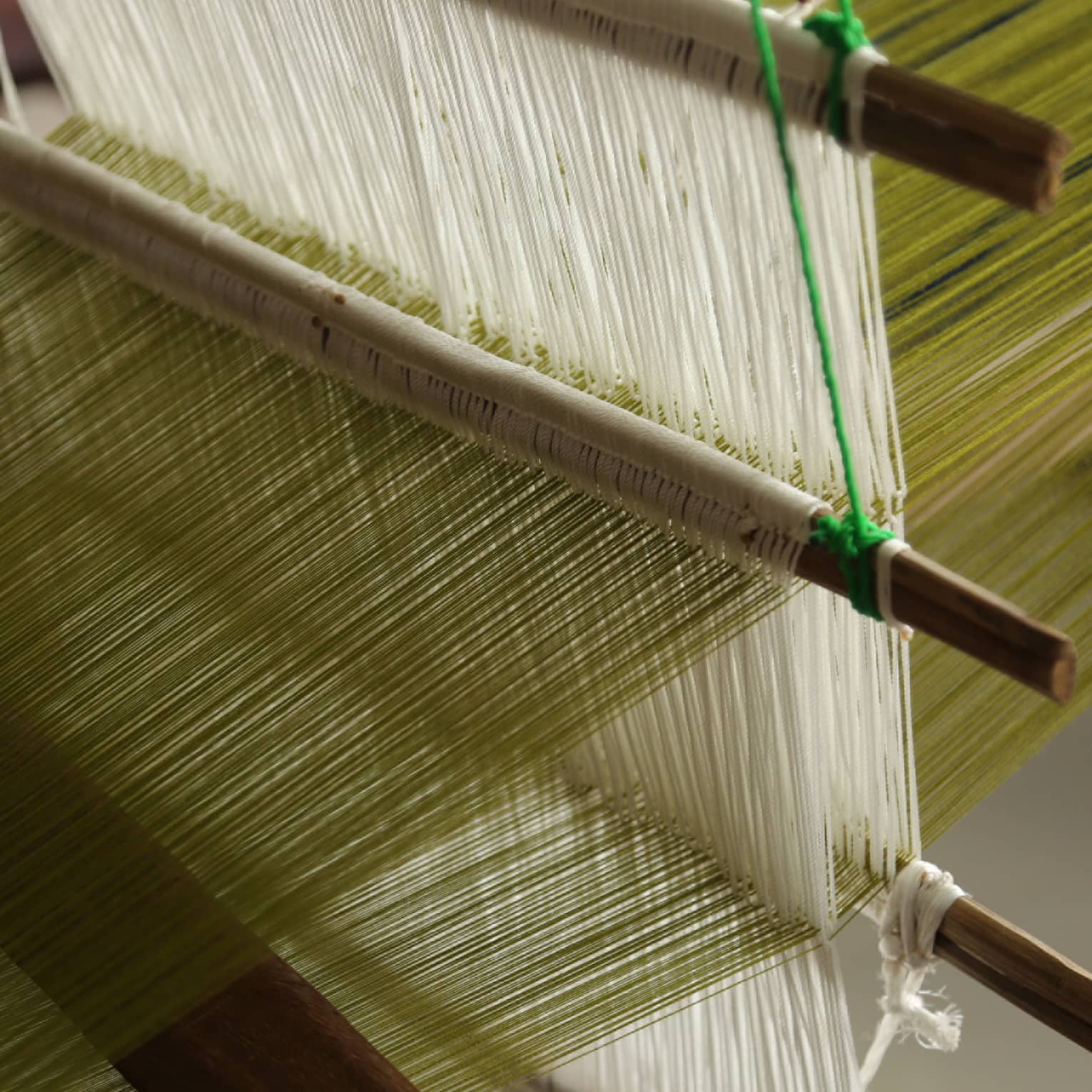 Close-up of green and white threads on a traditional handloom weaving machine