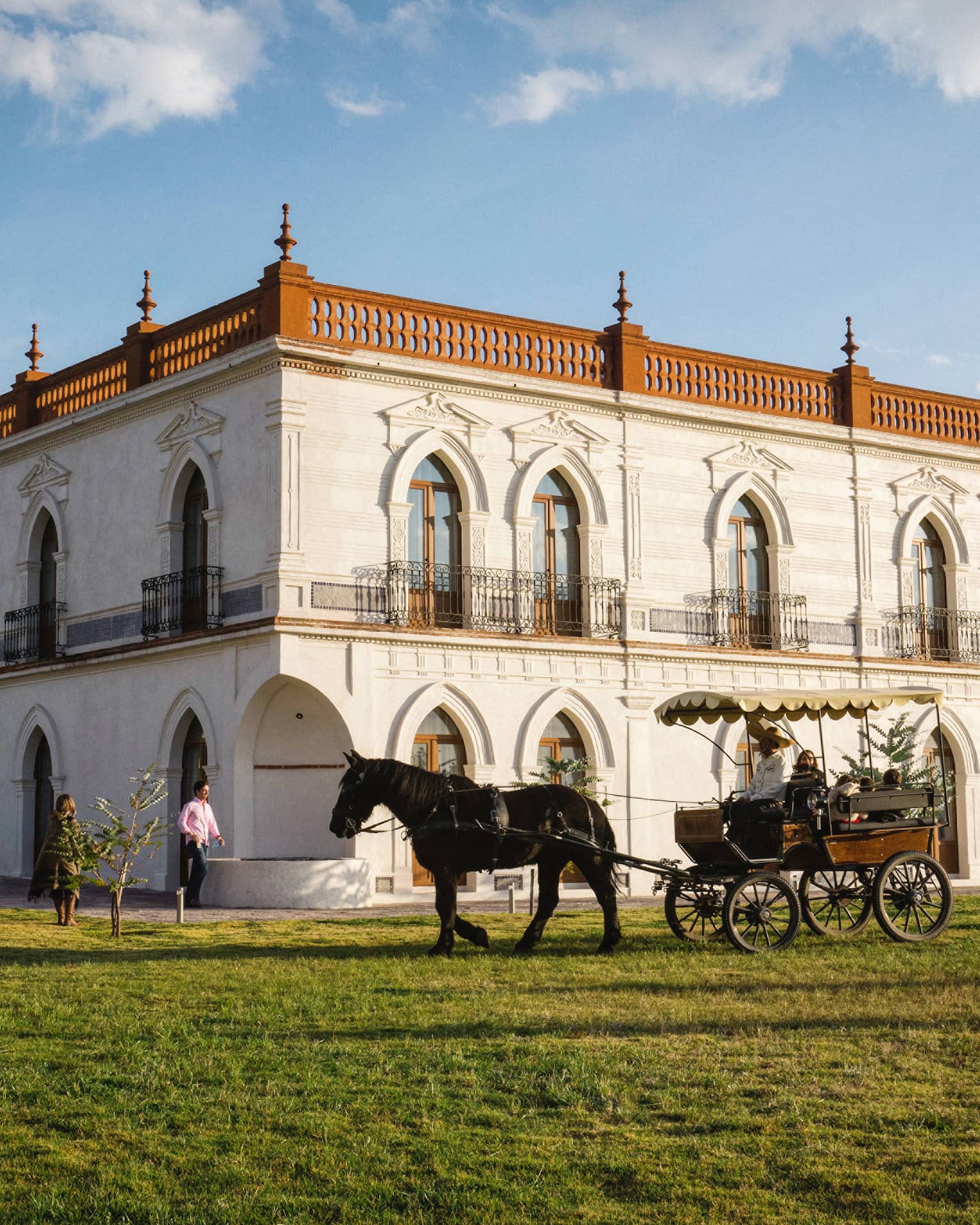 Guests enjoying a horse-drawn carriage ride around a large white building with several beautifully carved arched doorframes.