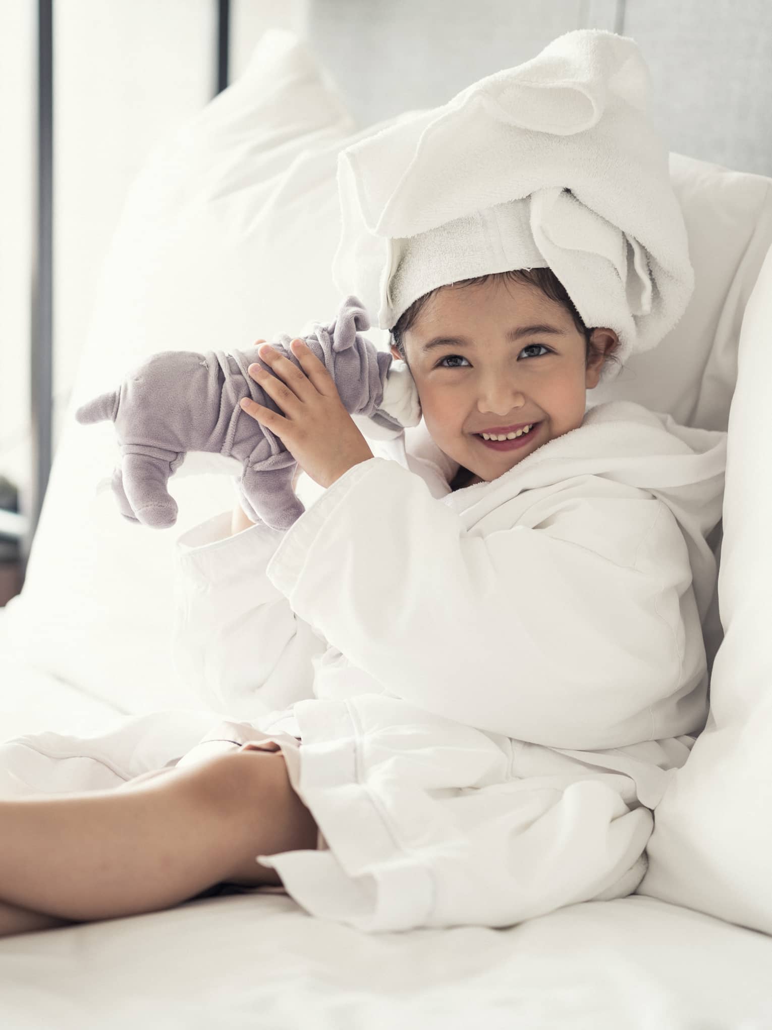 Smiling robe-clad young girl lounges on the bed with her stuffed animal