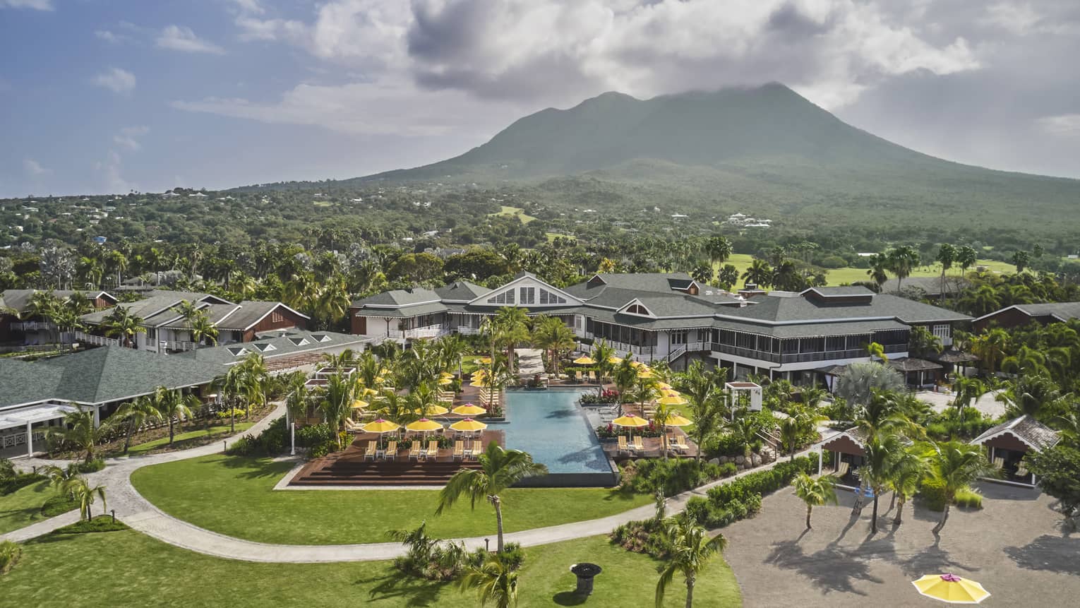 Aerial view of large pool area at Four Seasons Nevis, with yellow umbrellas, green grass, edge of beach