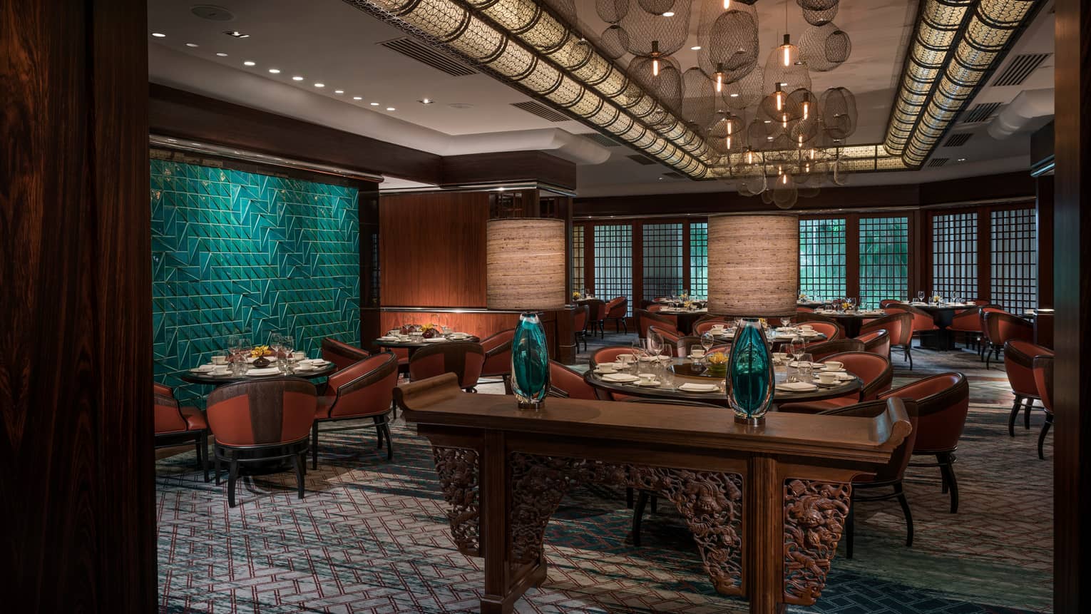 Carved wood console with glass vases in front of dining room, green tile wall