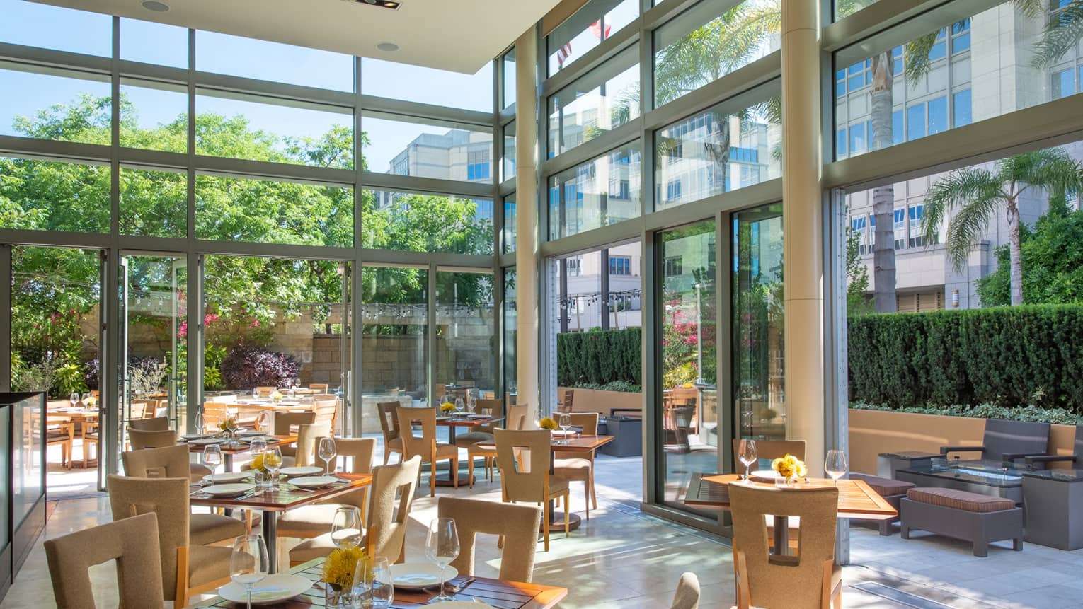A restaurant with sun coming in through large glass windows and walls.