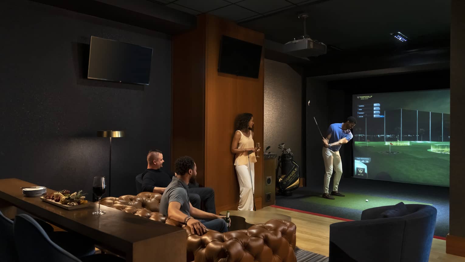 A group of people enjoying an indoor golf simulator experience at the luxury hotel Topgolf Swing Suite, with plush seating and a relaxed atmosphere